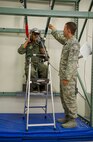 Kirby Balinski, a teenager battling Hodgkin’s Lymphoma, hangs in a virtual reality parachute trainer as Staff Sgt. Jeffrey Ray, 15th Operations Support Squadron survival, evasion, resistance and escape specialist, explains how  to use the equipment to maneuver to the ground after a simulated aircraft ejection during a tour of the 15th OSS Aircrew Flight Equipment section as part of the Pilot For a Day program at Joint Base Pearl Harbor-Hickam, Hawaii, May 29, 2014. (U.S. Air Force photo/Tech. Sgt. Terri Paden)