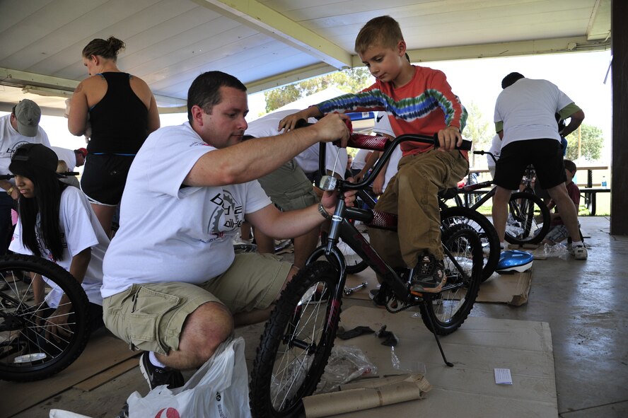 Quentin Salisbury, 7, son of Lt. Col. David Salisbury, 944th Operations Group commander, sits on his bike for the first time as a Build-A-Bike volunteer tightens screws and makes adjustments. (U.S. Air Force photo/Senior Airman Grace Lee)