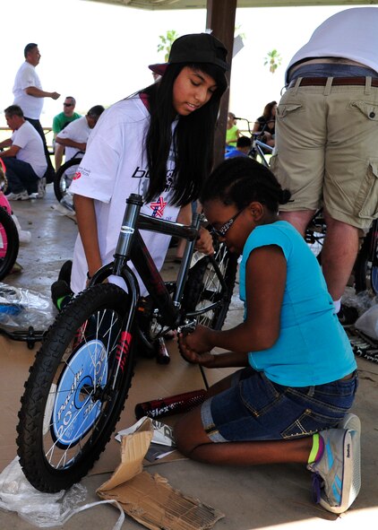 Alicia Ramirez, Build-A-Bike volunteer, helps Destinee Harris, 9, daughter of Tech. Sgt. Thomas Harris, 56th Civil Engineer Squadron electric shop NCO-in-charge, put pedals on her bike May 17 at Fowler Park on Luke Air Force Base. A sponsor supplied the materials needed to build the bike, in addition to the bike locks and helmets. (U.S. Air Force photo/Senior Airman Grace Lee)