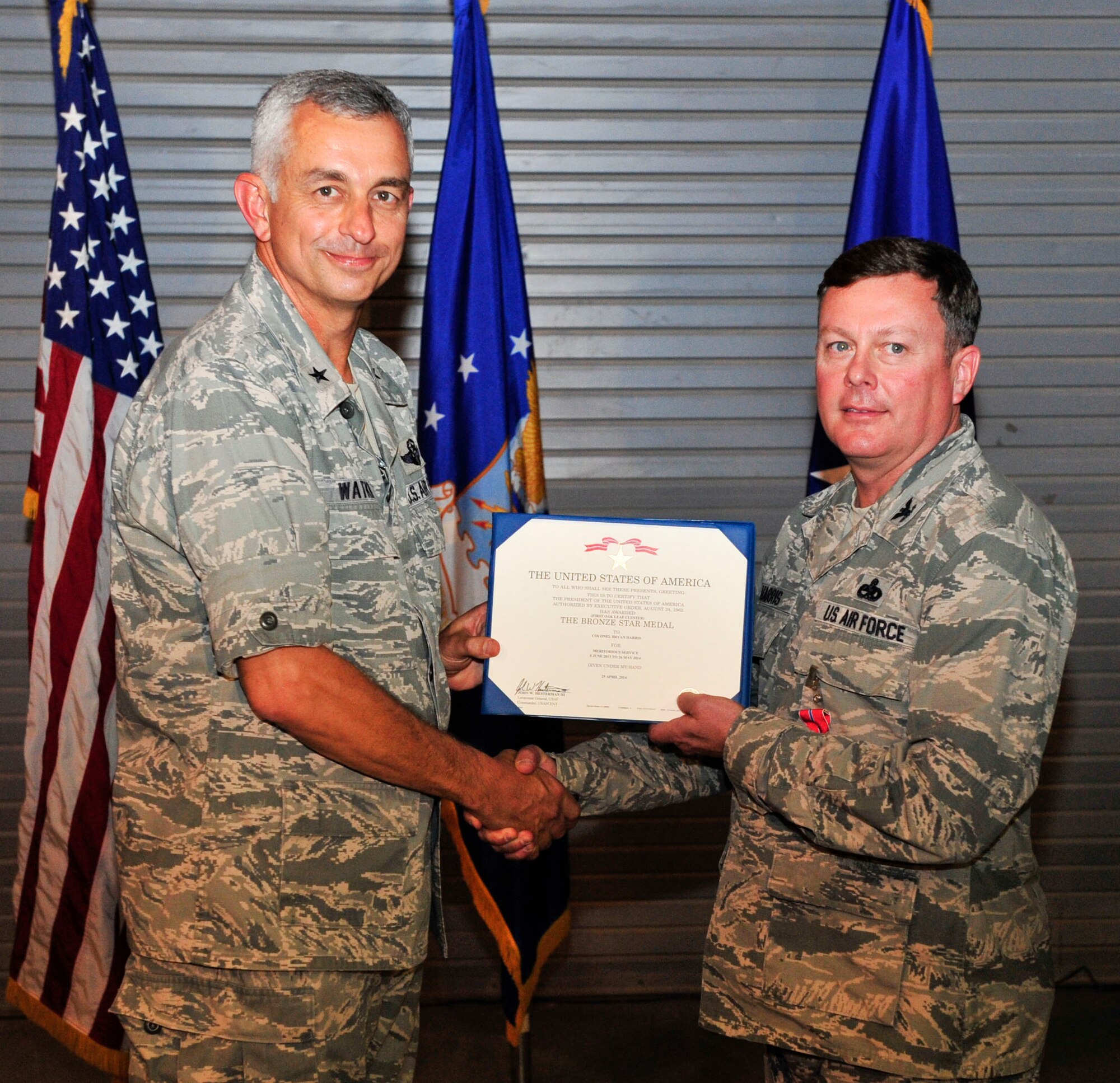 U.S. Air Force Brig. Gen. Roger Watkins 379th Air Expeditionary Wing commander and outgoing 379th Expeditionary Maintainence Group commander, Col. Bryan Harris, pose for a photo during Harris’s bronze star presention at Al Udeid Air Base, Qatar, May 26, 2014. Harris served as the 379th EMXG commander for the last year. leading a group consisting of 1,100-plus personnel performing combat sortie generation and providing aircraft/munitions capability. Harris is from Marshall, Texas (U.S. Air Force photo by Senior Airman Colin Cates)