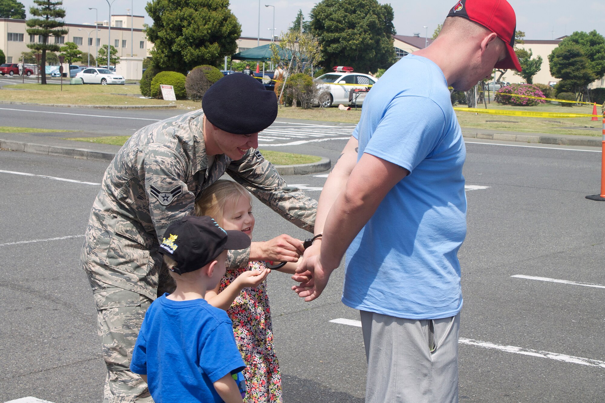 Airman 1st Class Quinton Lequieu, 374th Security Forces Squadron patrolman, helps children place handcuffs on Staff Sgt. Joseph Cull, 374th Security Forces Squadron NCO in charge of confinement, during Police Week at Yokota Air Base, Japan, May 19, 2014. Security Forces members used static displays and demonstrations to educate base personnel on law enforcement procedures. (U.S. Air Force photo by Airman 1st Class David Danford/Released)