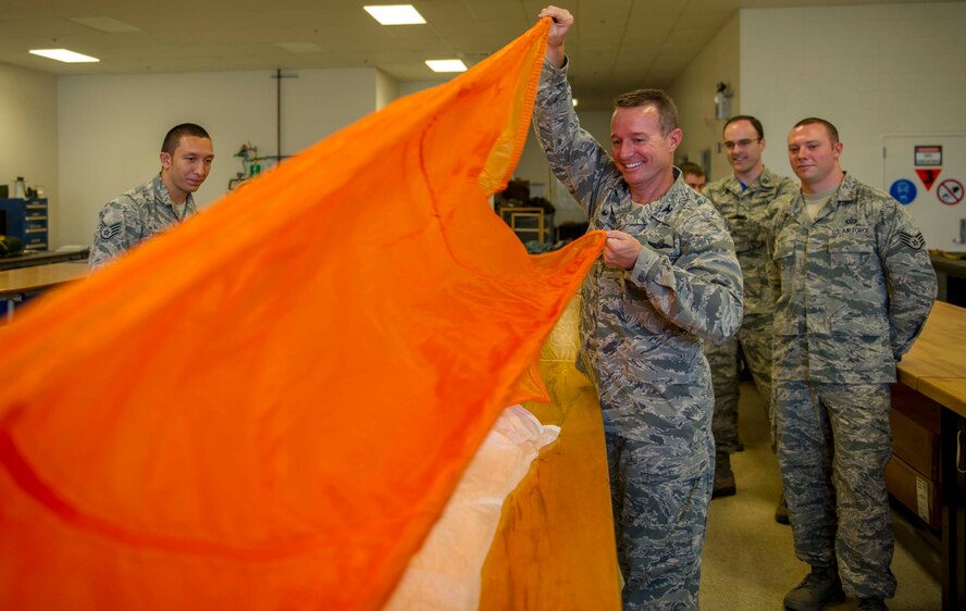Col. Randy Huiss, 15th Wing commander, folds a parachute canopy while his trainer, Staff Sgt. Julio Torres, 15th Operations Support Squadron Aircrew Flight Equipment main shop assistant NCO in charge, and other Airmen look on at Joint Base Pearl Harbor-Hickam, Hawaii, Oct. 24, 2014. (U.S. Air Force photo by Tech. Sgt. Terri Paden)