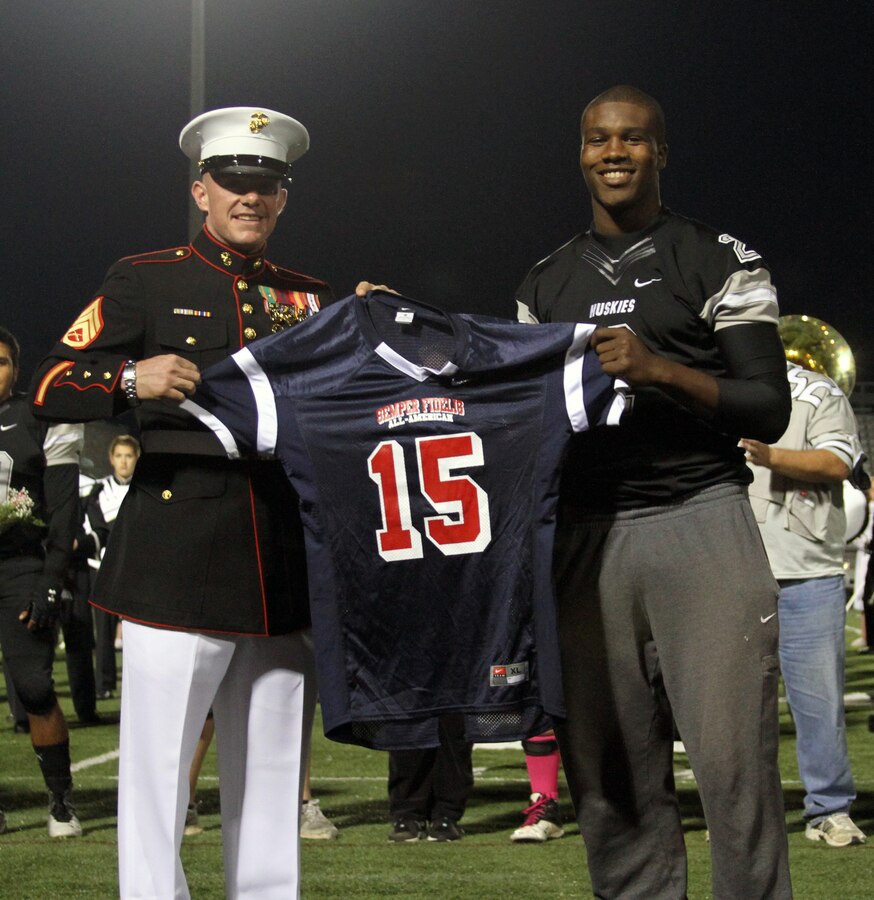 Staff Sgt. James Spence, canvassing recruiter, Marine Corps Recruiting Substation Charlotte presents Carl Tucker, senior, William A. Hough High School with his Semper-Fidelis All-American Bowl jersey before kick-off of his last home football game at William A. Hough High School on Oct. 31, 2014.