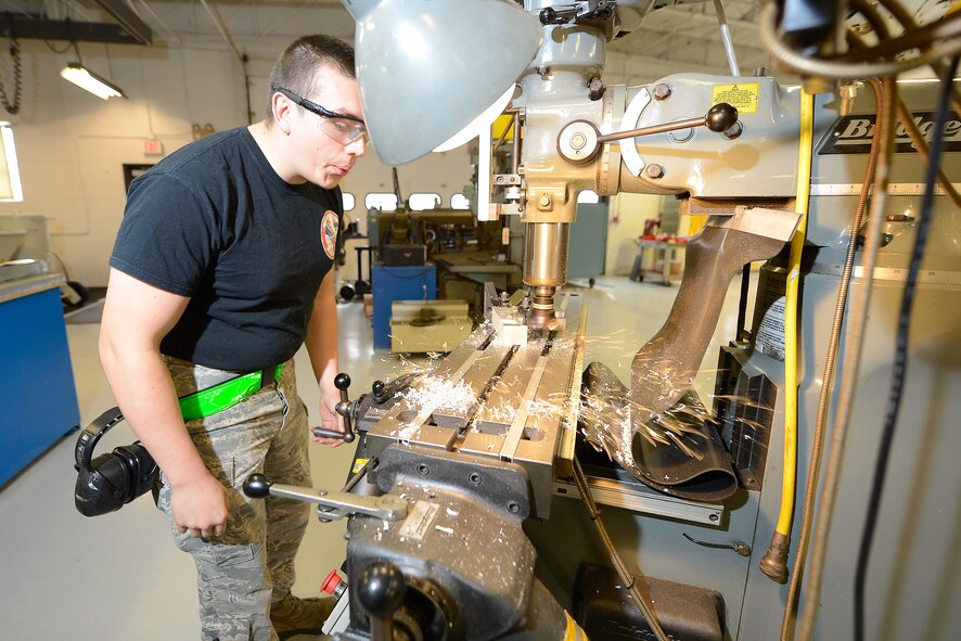 Airman 1st Class Matthew Mooneyham, 436th Maintenance Squadron aircraft metals technician journeyman, blows away aluminum shavings as he mills a block of aluminum inside the 436th Maintenance Squadron???s Aircraft Metals Technology Shop Oct. 31, 2014, at Dover Air Force Base, Del. Mooneyham wears protective eyewear and has hearing protection on his belt, if required, while working in the industrial setting. (U.S. Air Force photo/Greg L. Davis)
