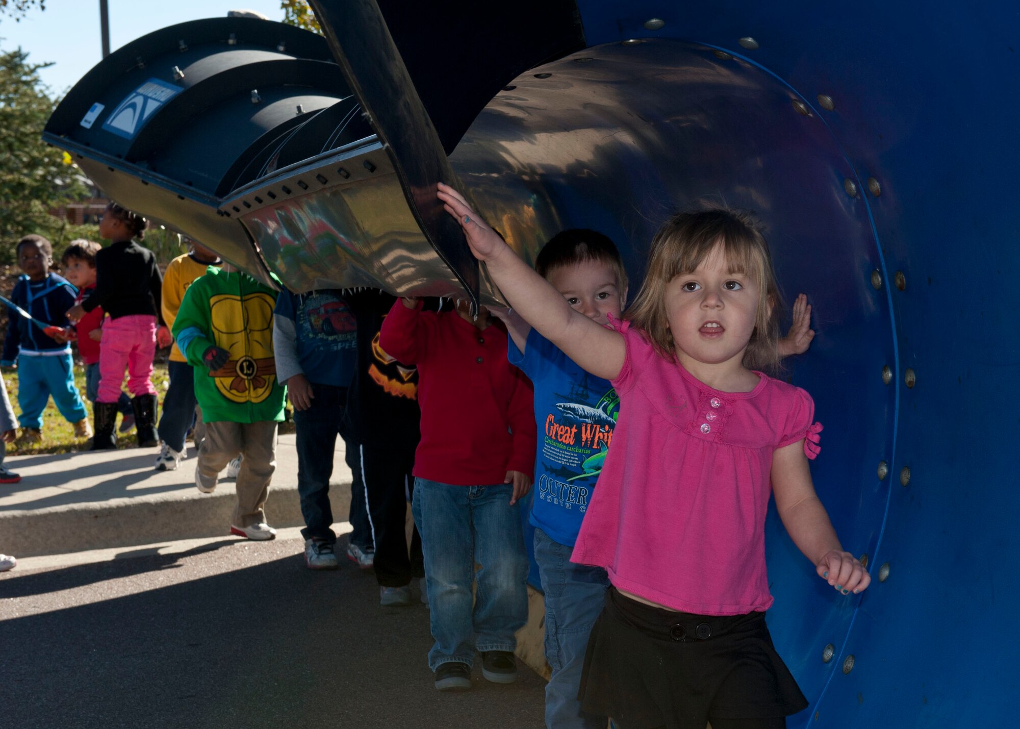 PETERSON AIR FORCE BASE, Colo. – Children from the main Child Development Center walk under the plow of the Oshkosh snow removal trucks to see how big they really are during the Snow Parade, which briefly stopped at the CDC, Oct. 28. The Snow Parade was held to familiarize and show off the snow plows, dump trucks, fire trucks and other equipment to base personnel and their families. The children also were able to hang out with Santa who rode in on the fire truck to greet them. (U.S. Air Force photo/Airman 1st Class Rose Gudex)