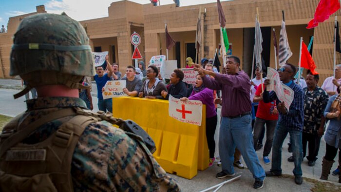 Role players protest outside of a simulated embassy while a Marine with Echo Company, 2nd Battalion, 8th Marine Regiment, 2nd Marine Division stands guard at a Military Operations on Urban Terrain town aboard Marine Corps Base Camp Lejeune, N.C., Oct. 30, 2014. The Marines provided security for the embassy as part of an embassy reinforcement operation in conjunction with Exercise Bold Alligator 2014. Bold Alligator is a scenario-driven, simulation-supported, amphibious assault exercise and is the largest exercise held on the East Coast. The exercise is scheduled to be conducted through Nov. 10. The battalion is participating in the exercise to prepare for the unit’s upcoming deployment as the ground combat element for the Black Sea Rotational Force.