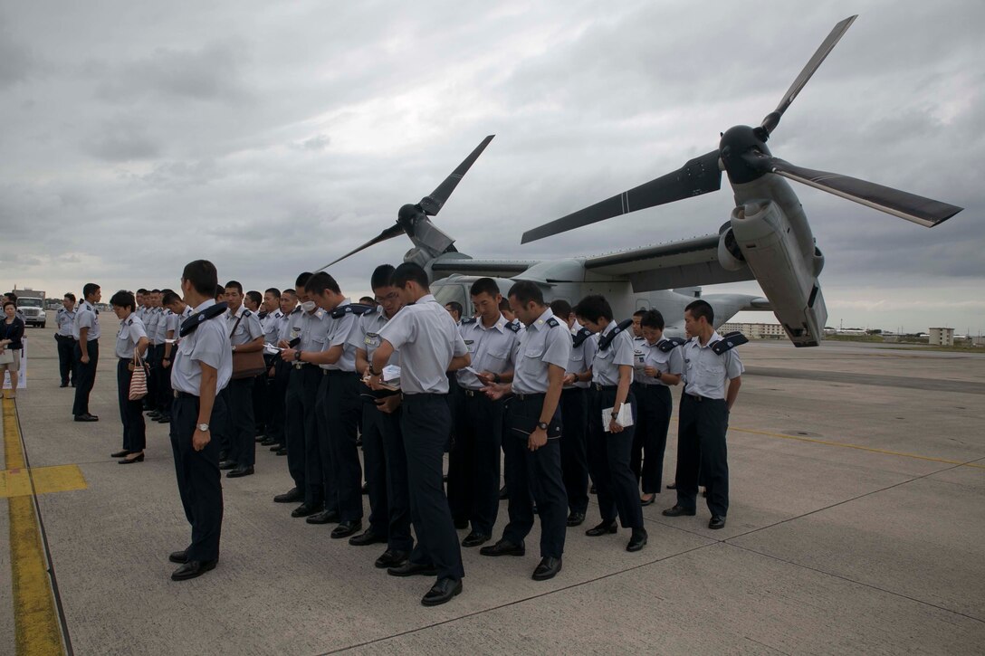 Japan Air Self-Defense Force service members stand in formation in front of an MV-22B Osprey tiltrotor aircraft Oct. 30 at Marine Corps Air Station Futenma. Following the flight simulator, the JASDF service members travelled to the flight line where there was an Osprey set up for display. The JASDF service members are students at the JASDF Air Officer Candidate School. The Osprey is assigned to Marine Medium Tiltrotor Squadron 265, Marine Aircraft Group 36, 1st Marine Aircraft Wing, III Marine Expeditionary Force. 