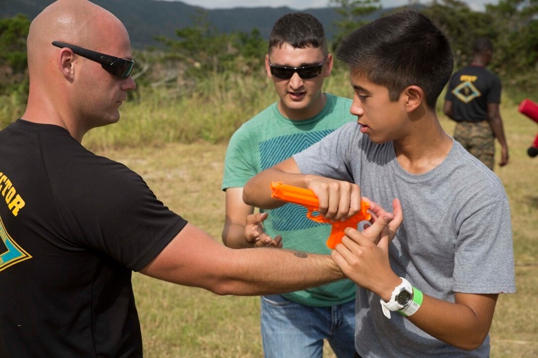 Donald W. Christensen, right, learns to disarm a weapon from Cpl. Ryan T. Starr Oct. 25 during Junglefest 2014 at the Jungle Warfare Training Center on Okinawa, Japan. The festival allowed Okinawa community members and U.S. service members to see and experience some of the military training techniques that the instructors at the JWTC teach during the jungle survival training course. Christensen is a student  and child of an active duty service member on Okinawa. Starr, from Waldron, Arkansas, is an instructor at the Jungle Warfare Training Center.  (U.S. Marine Corps photo by Lance Cpl. Matt Myers/Released)