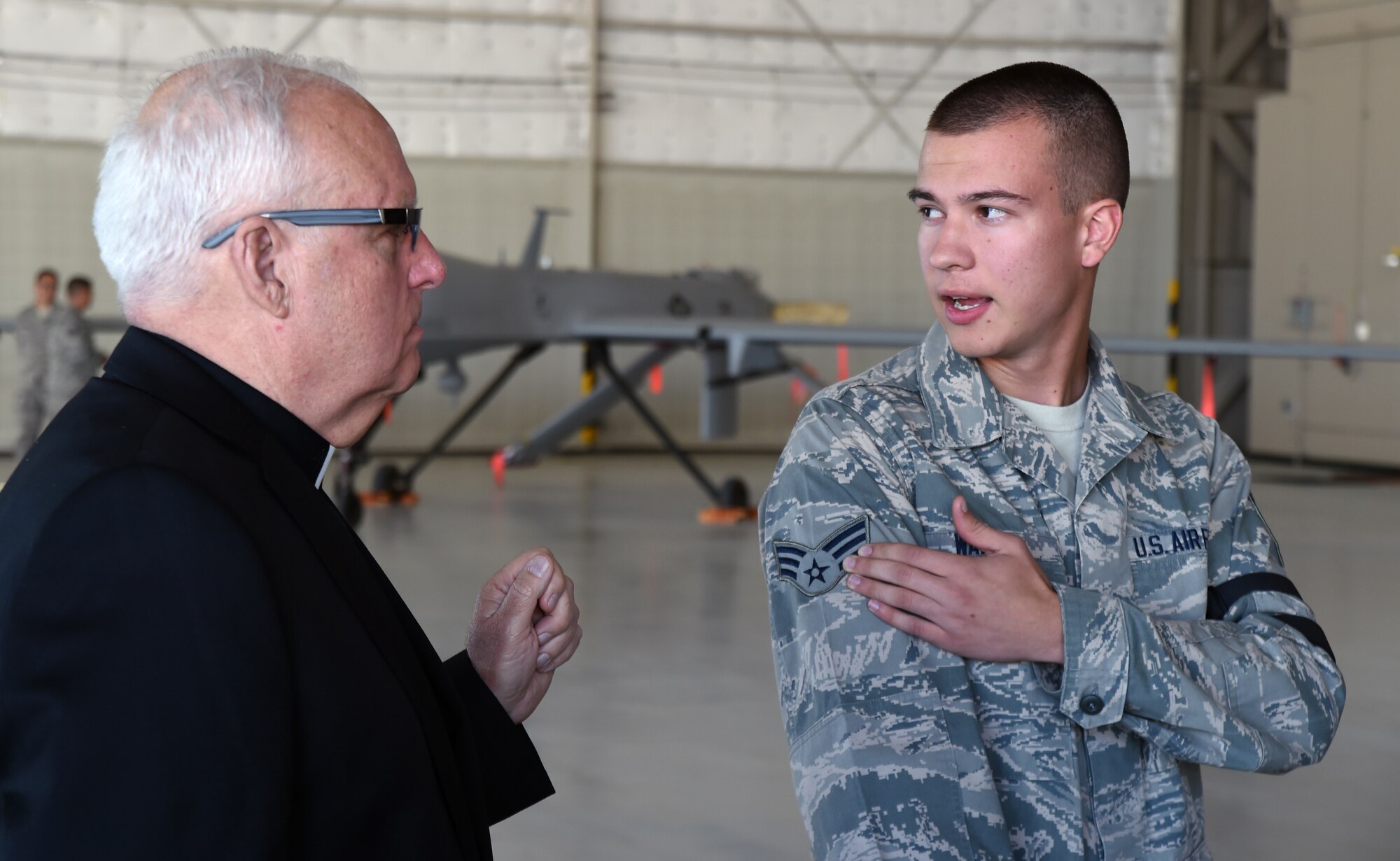 Father John Kinney, retired chaplain (Lt. Col.), and Senior Airman Kyle Walsh, 432nd Aircraft Maintenance Squadron MQ-9 Reaper crew chief, discuss enlisted rank structure during a “Come Be With Us” chaplain recruiting tour at Creech Air Force Base, Oct. 28, 2014. The Chaplain Corps held the annual tour to introduce potential Air Force recruits to military culture. (U.S. Air Force photo by Tech. Sgt. Shad Eidson/Released)