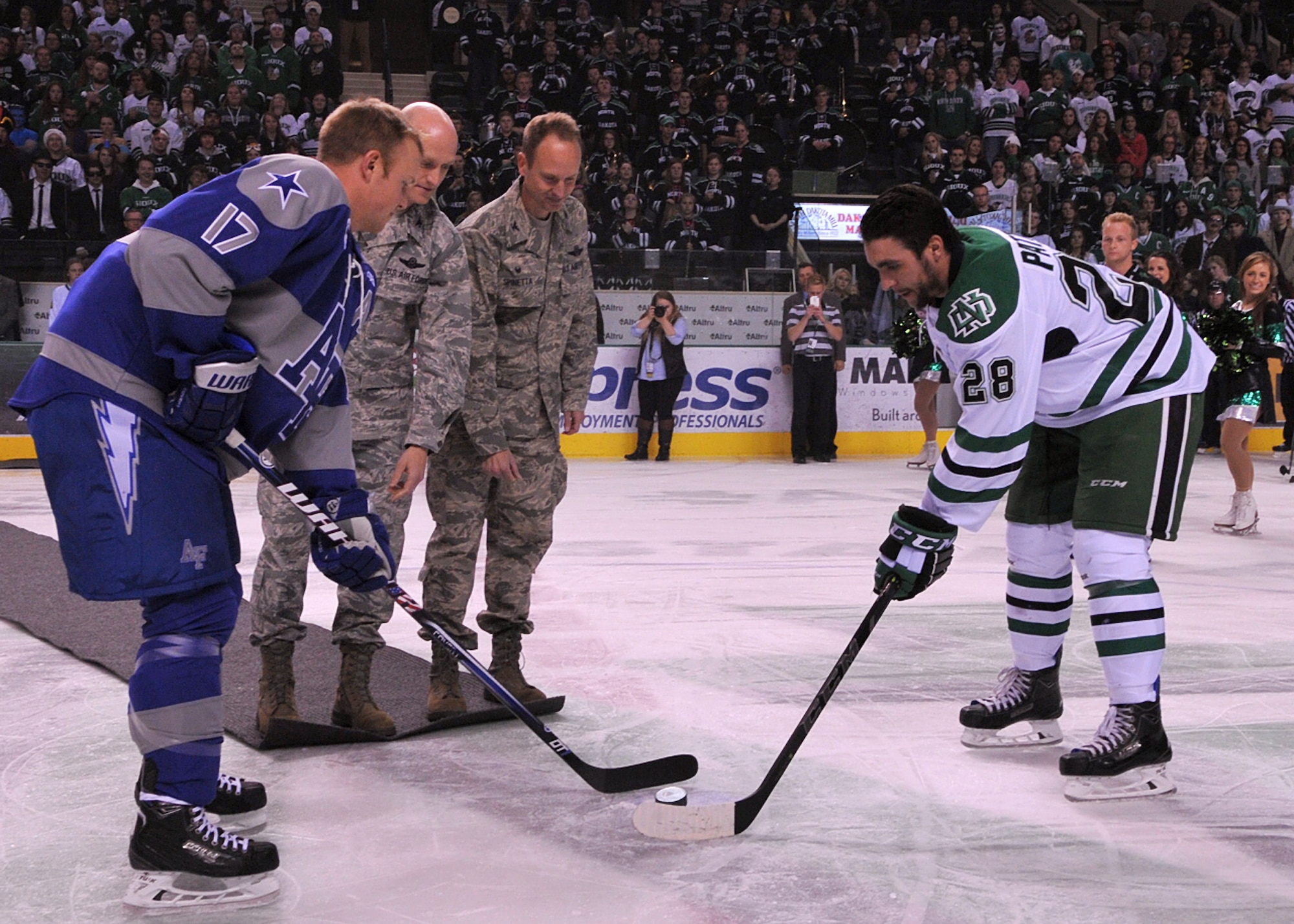 Col. Robert Cook, 319th Air Base Wing vice commander, and Col. Lawrence Spinetta, 69th Reconnaissance Group commander, drop the ceremonial first puck to begin the Air Force Academy vs. University of North Dakota Hockey Hall of fame game Nov. 1, 2014, at the Ralph Engelstad Arena in Grand Forks, N.D. The ceremonial first puck is a longstanding hockey tradition that signifies the end of the pregame activities and the beginning of the game. The ceremonial puck is then given to the individual who dropped the puck. (U.S. Air Force photo/Airman 1st Class Bonnie Grantham)