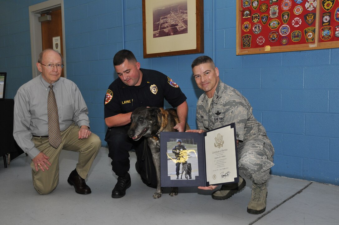 Arnold Police K-9 Officer Bikkel accepts a U.S.  Air Force Certificate of Service from Arnold Engineering Development Complex (AEDC) Commander Col. Raymond Toth (right) during Bikkel’s retirement celebration on Oct. 21. ATA Mission Support Department Director Pat Eagan (left) and Arnold Police Officer Jason Layne accompany Bikkel. (Photo by Rick Goodfriend)