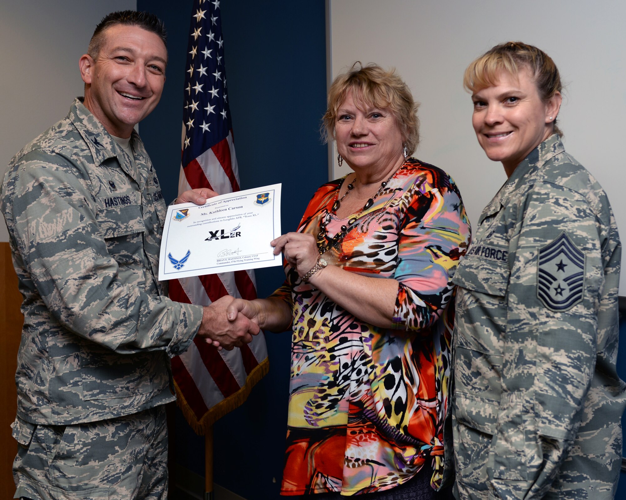 Kathleen Carson, center, 47th Contracting Flight contract specialist, poses with Col. Brian Hastings, left, 47th Flying Training Wing commander, and Chief Master Sgt. Teresa Clapper, right, 47th FTW command chief, after being presented the XLer of the week award here Nov. 4, 2014. The XLer is a weekly award chosen by wing leadership and is presented to those who consistently make outstanding contributions to their unit and Laughlin. (U.S. Air Force photo by Airman 1st Class Jimmie D. Pike)(Released)