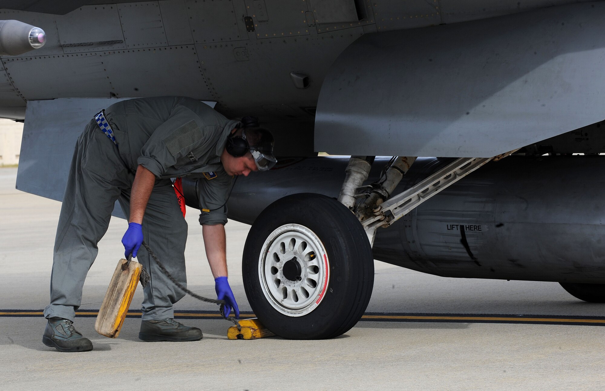 U.S. Air Force Senior Airman Ethan Edmisten, 20th Aircraft Maintenance Squadron dedicated crew chief, sets a pair of wheel chocks to secure an F-16CM Fighting Falcon for hot pit refueling at Shaw Air Force Base, S.C., Nov. 5, 2014. Wheel chocks are used to secure aircraft when they are parked. (U.S. Air Force photo by Airman 1st Class Michael Cossaboom/Released)