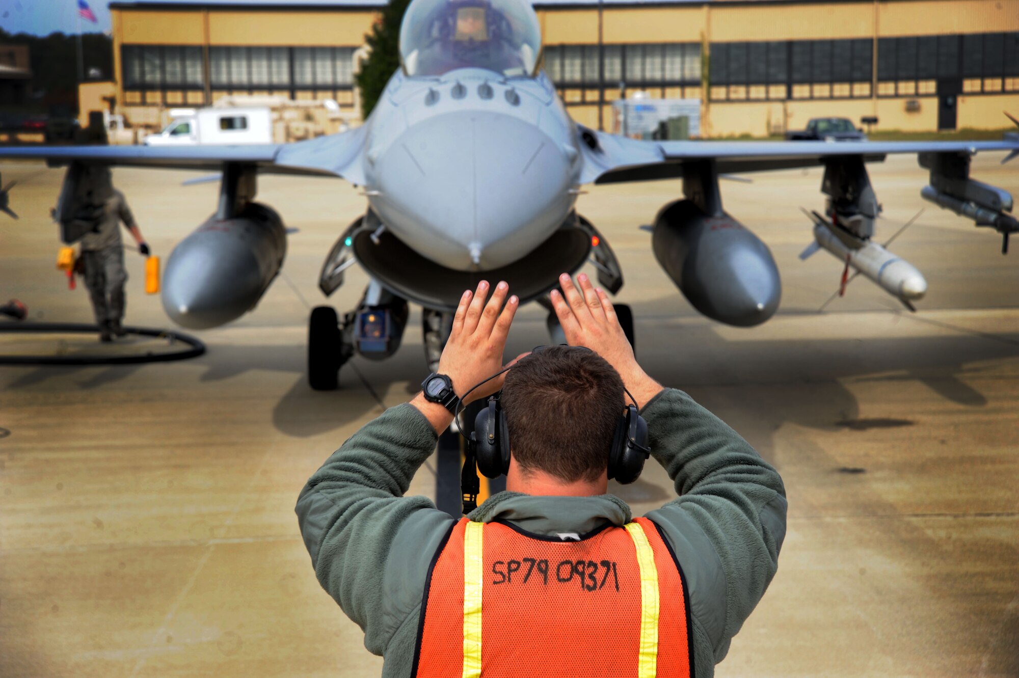 A U.S. Air Force Airman assigned to the 20th Aircraft Maintenance Squadron marshals an F-16CM Fighting Falcon during hot pit refueling at Shaw Air Force Base, S.C., Nov. 5, 2014.  During hot pit refueling, three Airmen work togther to inspect the jet for damage, then refuel it and get it back into the air as quickly as possible. (U.S. Air Force photo by Airman 1st Class Michael Cossaboom/Released)
