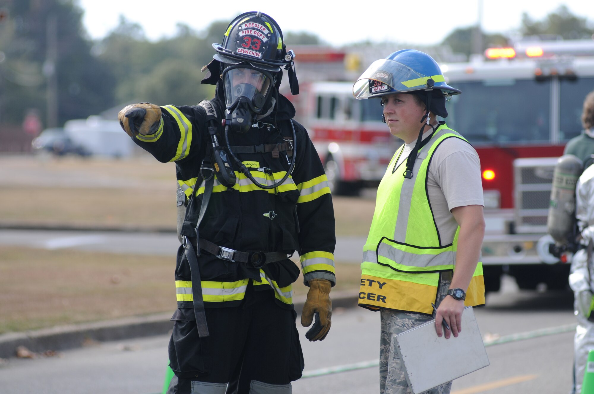Staff Sgts. John Hood and Jerrod Lott, Keesler firefighters, discuss the setup and location of the decontamination site during a hazardous material exercise scenario Nov. 5, 2014, at the Taylor Logistics Center, Keesler Air Force Base, Miss.  The exercise scenario began with an Airman accidentally hitting a 55-gallon drum of sulfuric acid with a forklift and knocking several more drums off of a truck causing the liquid to splash onto other Airmen.  Immediately, the Airmen simulated skin and eye burns from exposure to the agent, while additional Airmen on the loading dock started coughing and experiencing shortness of breath. (U.S. Air Force photo by Kemberly Groue)