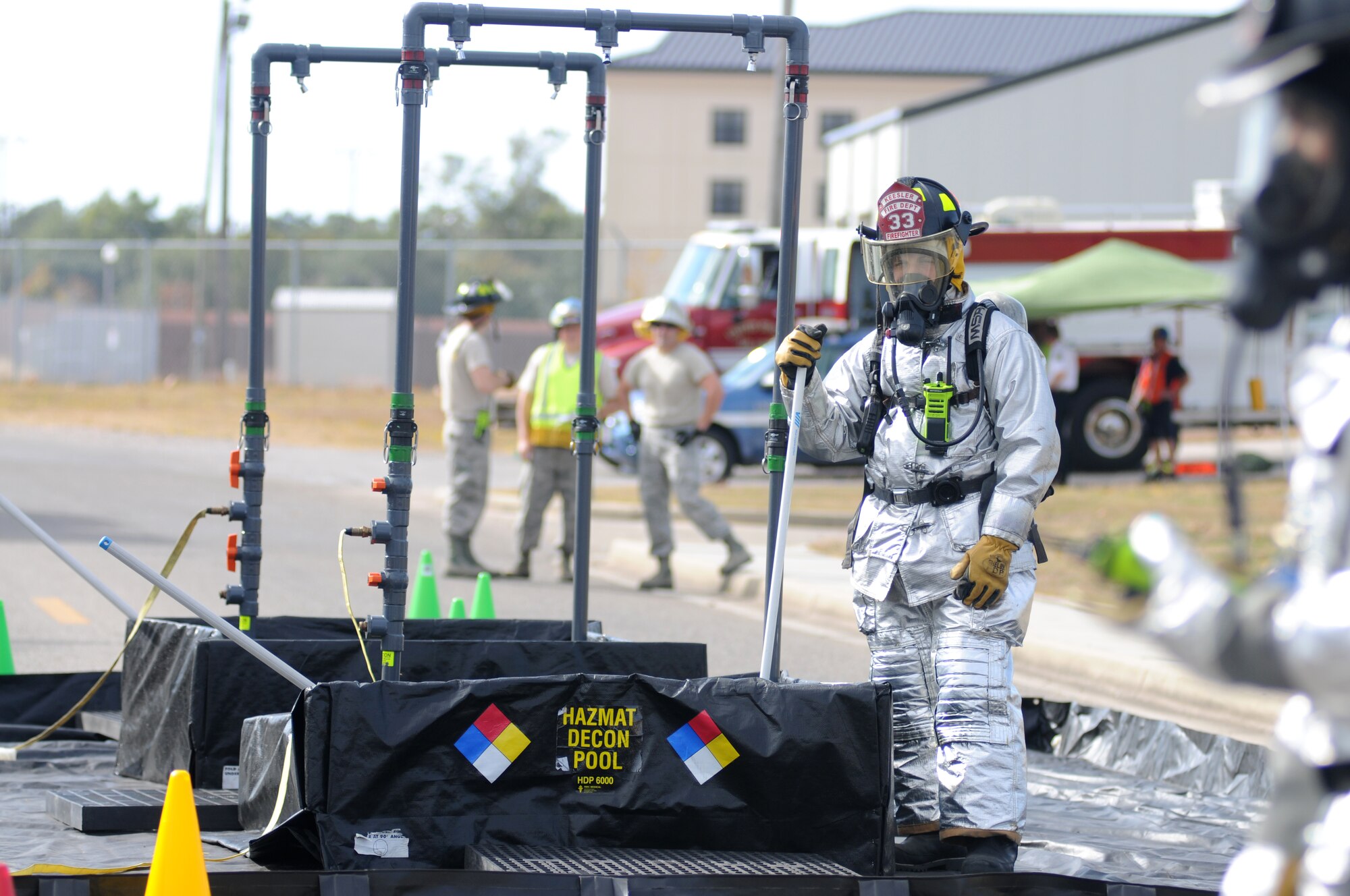 Airman 1st Class Jacob Linton, Keesler firefighter, prepares to decontaminate “victims” as they leave a contaminated area during a hazardous material exercise scenario Nov. 5, 2014, at the Taylor Logistics Center, Keesler Air Force Base, Miss.  The exercise scenario began with an Airman accidentally hitting a 55-gallon drum of sulfuric acid with a forklift and knocking several more drums off of a truck causing the liquid to splash onto other Airmen.  Immediately, the Airmen simulated skin and eye burns from exposure to the agent, while additional Airmen on the loading dock started coughing and experiencing shortness of breath. (U.S. Air Force photo by Kemberly Groue)
