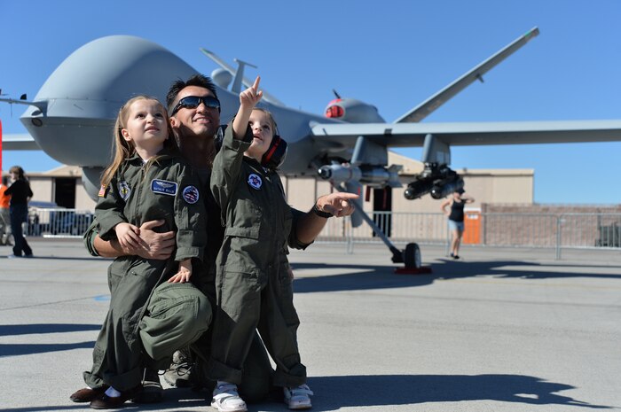 Natalie and Melanie watch the Legacy Bombers fly with their father Capt. Eric for the friends and family day at the 2014 Open House on Nellis Air Force Base, Nev., Nov. 7, 2014. The Open House is a two-day event that will depict the history of American aviation and salute recent accomplishments of America's military in operations around the globe through numerous military and civilian ground displays. (Names withheld for security)