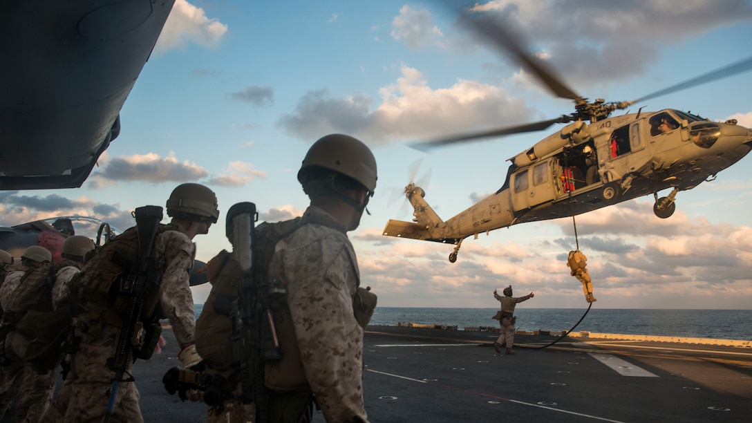 Marines with Security Platoon, Maritime Raid Force, 24th Marine Expeditionary Unit, watch a fellow Marine fast-rope out of an MH-60S Seahawk helicopter on the flight deck of the USS Iwo Jima, Oct. 31, 2014. The MRF conducted fast-rope training using aviation support from Sea Combat Squadron 28. The 24th MEU is participating in exercise Bold Alligator, an exercise intended to improve Navy and Marine Corps amphibious core competencies. 