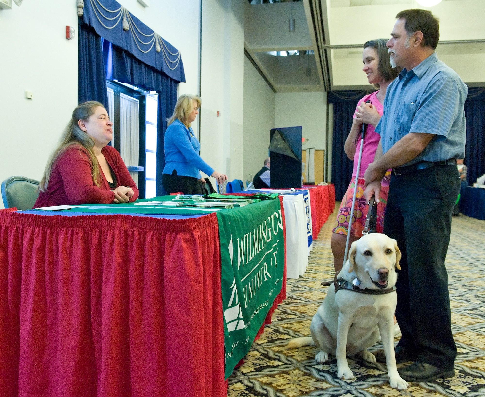 Lloyd Schmitz, National Disability Employment Awareness Month Luncheon guest speaker, right, and his wife Kathleen, talk with Cindy Webb, Wilmington University site associate during the Exceptional Family Member Program Information Fair Oct. 28, 2014, at The Landings on Dover Air Force Base, Del. The Schmitz’s, who are both visually impaired to different degrees, brought Lloyd’s Leader dog, Sophie, a four-year old Yellow Labrador Retriever. (U.S. Air Force photo/Roland Balik)