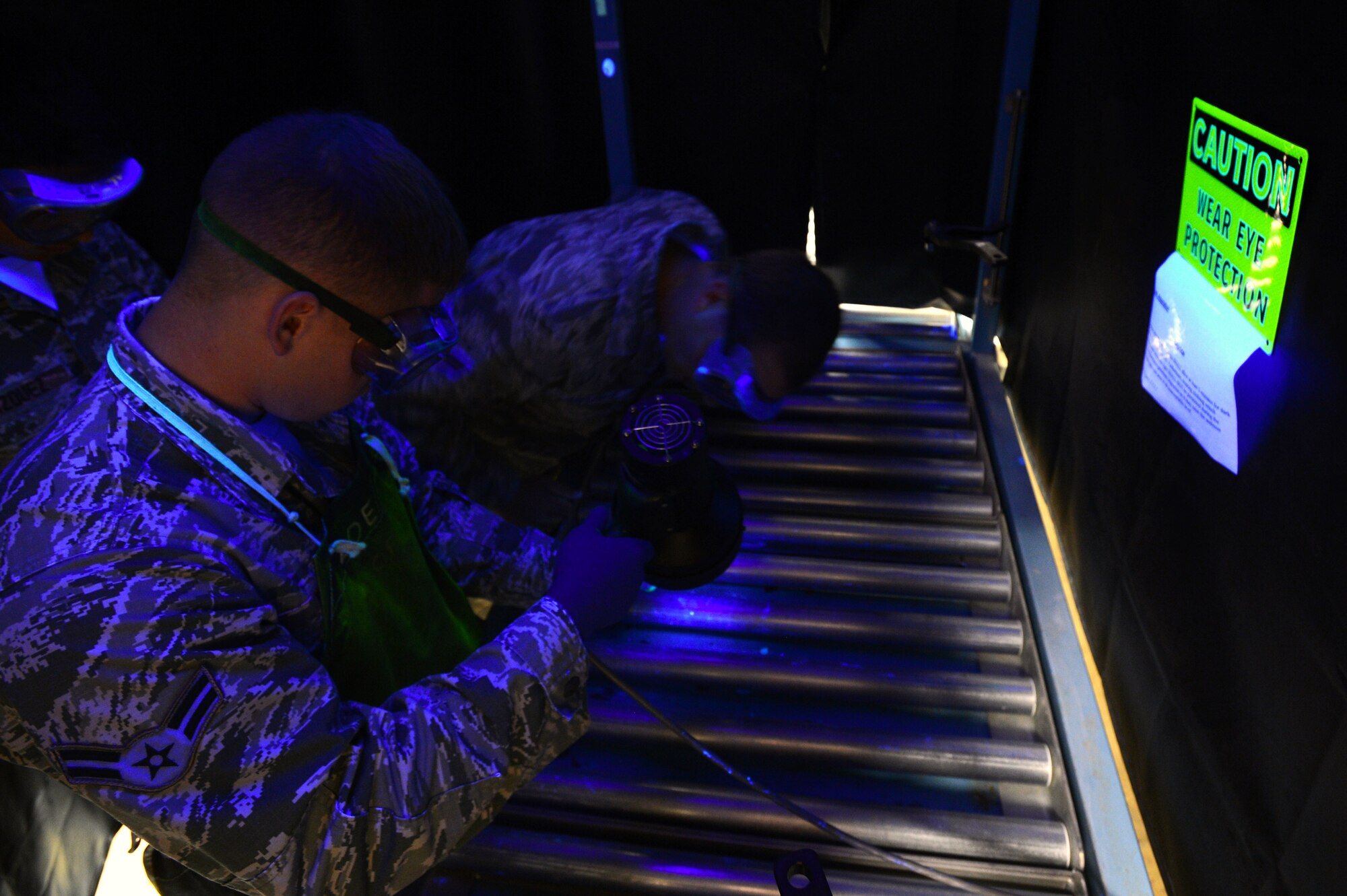 U.S. Air Force Airman 1st Class Logan Young and Senior Airman Zachary Applegate, 20th Equipment Maintenance Squadron non-destructive inspection technicians, search for cracks in an F-16CM Fighting Falcon wing attachment bolt at Shaw Air Force Base, S.C., Nov. 3, 2014. After processing through the magnetic particle machine, the bolt was inspected for cracks under a black light. (U.S. Air Force photo by Airman 1st Class Jensen Stidham/Released)  