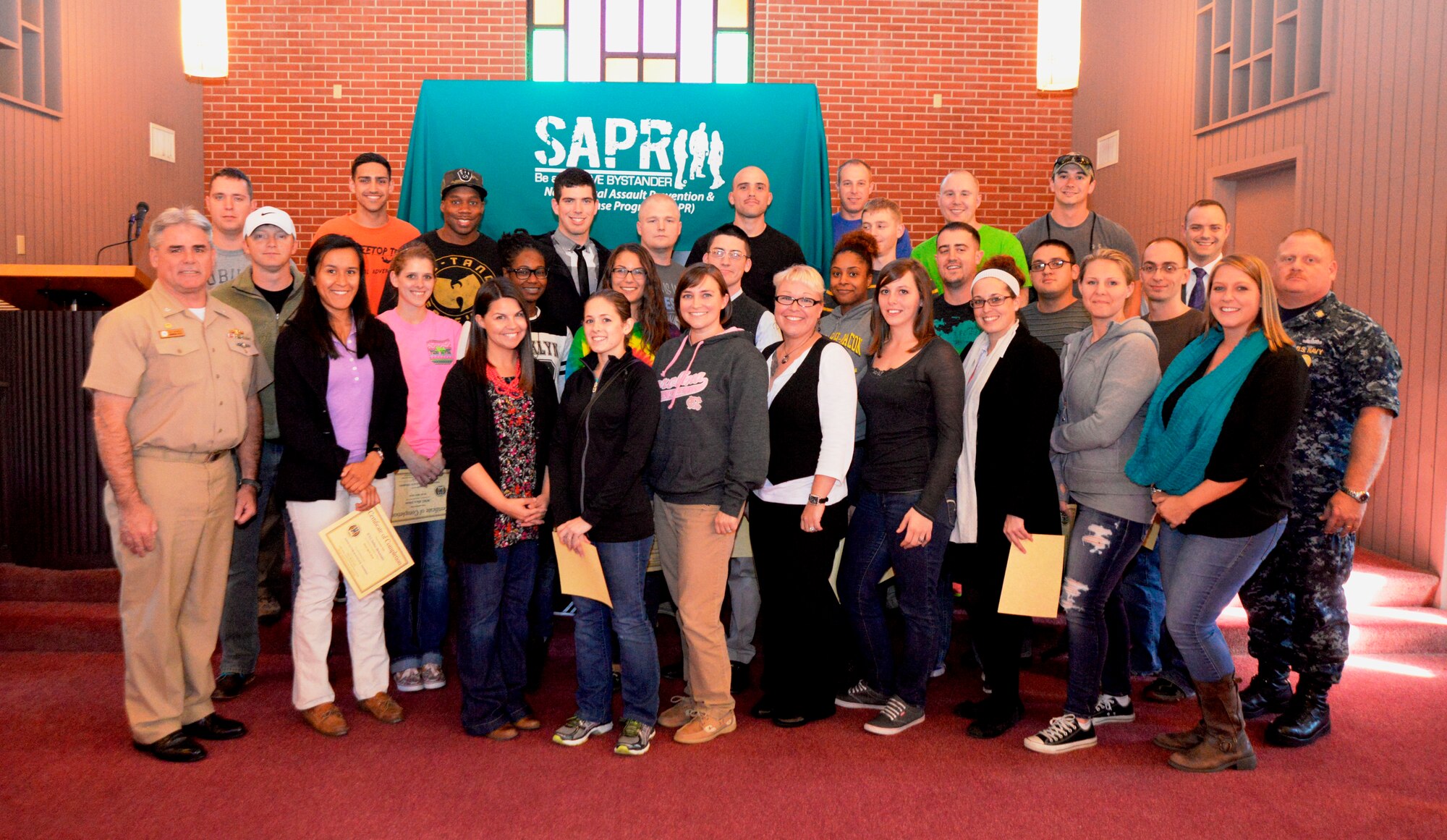Captain Timothy Sparks, Naval Support Activity commanding officer (left) and Tiffany Mizzell, Naval Weapons Station Sexual Assault Response Coordinator (third from left), along with  Master Chief Petty Officer Joseph Gardner, Naval Support Activity command master chief (right) and Ruby Godley, Naval Weapons Station civilian victim advocate, welcome 27 unit victim advocates to the Joint Base Charleston Weapons Station SAPR program after they completed 40 hours of sexual assault prevention and response victim advocate training Nov. 7, 2014, at Joint Base Charleston, S.C. (U.S. Air Force photo/Eric Sesit)