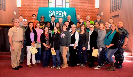 Captain Timothy Sparks, Naval Support Activity commanding officer (left) and Tiffany Mizzell, Naval Weapons Station Sexual Assault Response Coordinator (third from left), along with  Master Chief Petty Officer Joseph Gardner, Naval Support Activity command master chief (right) and Ruby Godley, Naval Weapons Station civilian victim advocate, welcome 27 unit victim advocates to the Joint Base Charleston Weapons Station SAPR program after they completed 40 hours of sexual assault prevention and response victim advocate training Nov. 7, 2014, at Joint Base Charleston, S.C. (U.S. Air Force photo/Eric Sesit)