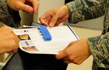 U.S. Air Force Staff Sgt. Taniah Otis (right), 18th Medical Support Squadron NCO in-charge of microbiology, assists Senior Airman Aaron Coonts (left), 18th Operation Support Squadron air traffic control journeyman, with placing the cotton swabs with his DNA in his application for the C.W. Bill Young Department of Defense Marrow Donor Program on Kadena Air Base, Japan, Nov.4, 2014. The applications are sent to the program where the DNA is collected, tested and stored in a database for future use. (U.S. Air Force photo by Airman 1st Class Keith James/Released)