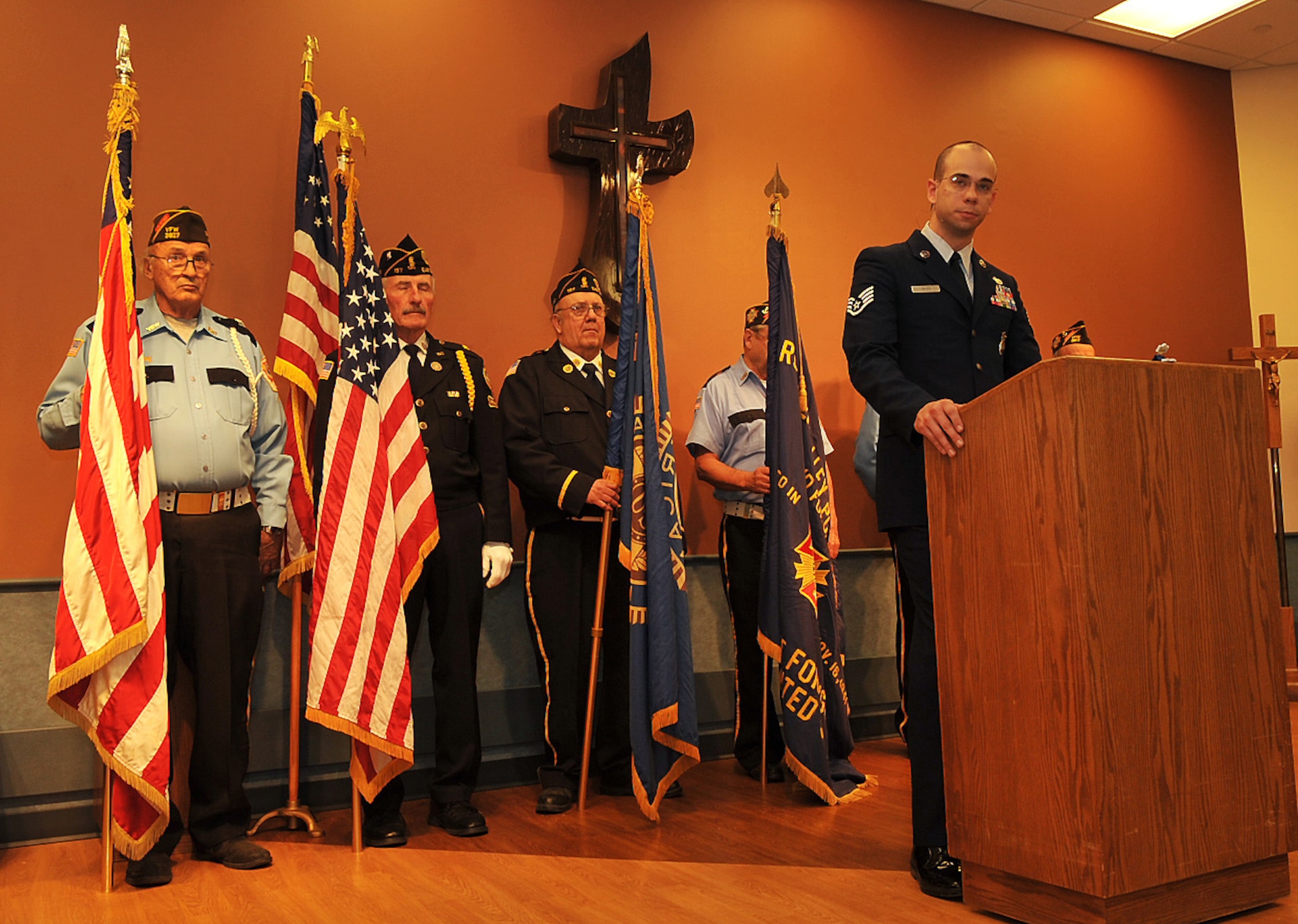 Staff Sgt. Christopher Giles, 319th Security Forces NCO-in-charge of security training, gives a Veterans Day speech as members of the American Legion Post 157 Honor Guard of East Grand Forks, Minn., stand with their flags at the Valley Elder Care Center Veterans Day program Nov. 11, 2014, in Grand Forks, N.D. There were approximately 120 people in attendance for Giles’ speech including 40 veterans who received certificates of appreciation for their service. (U.S. Air Force photo/Airman 1st Class Bonnie Grantham)