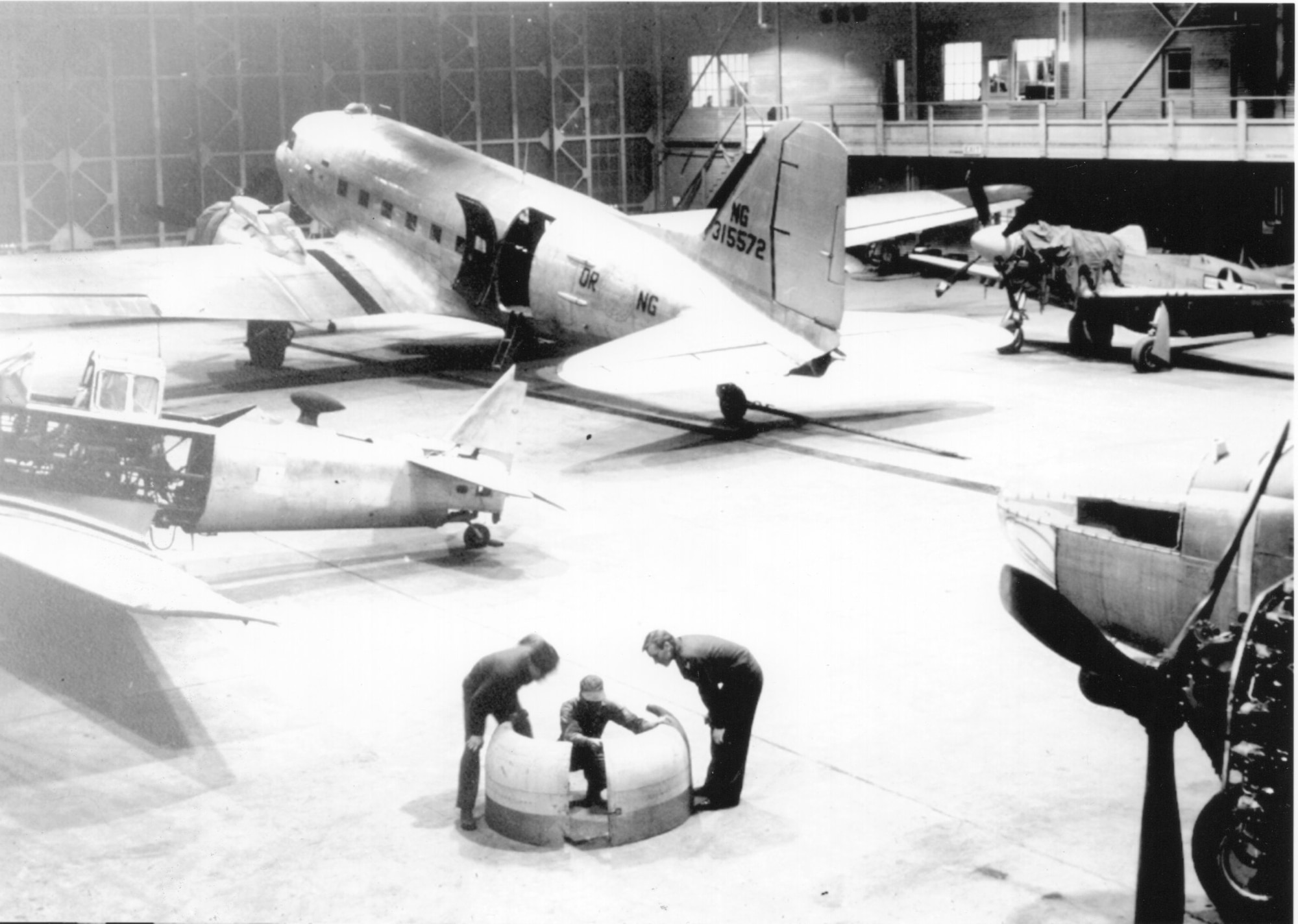 Aircraft of the Oregon (Air) National Guard in the immediate post-World War II period undergo maintenance at Portland Air Base, circa 1947.  Seen clockwise starting at the top are a C-47A Skytrain transport, P-51D Mustang fighter, A-26C Invader attack bomber and AT-6C Texan trainer.  The lack of national insignia on the C-47 is indicative of the transition period for Guard aircraft markings seen as the ANG re-established itself after WWII.   Perhaps a Caretaker is busy showing the other men in the picture a point about aircraft maintenance.  (Courtesy 142nd Fighter Wing History Archives)