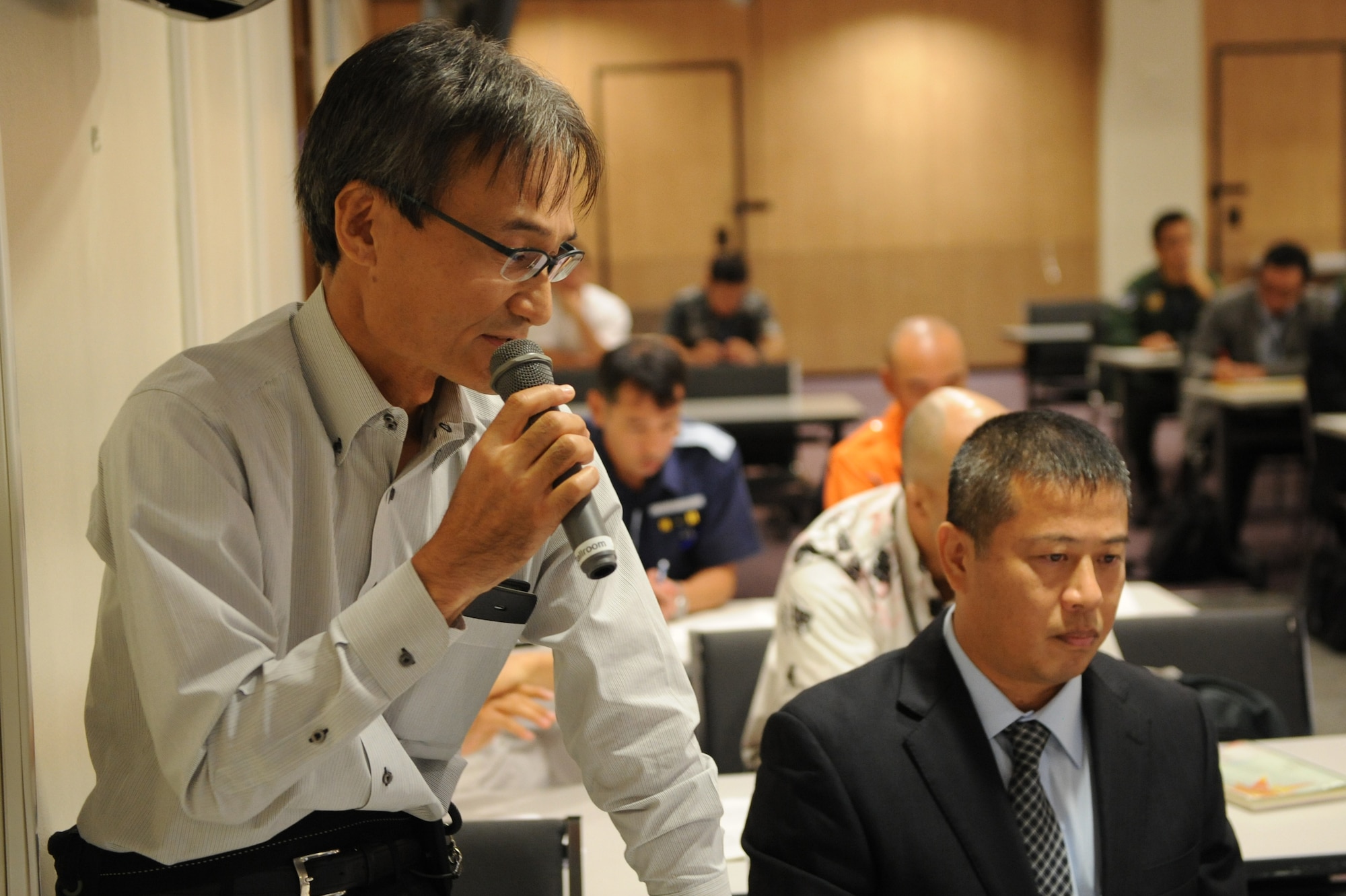 Noritomi Kikuzato, Okinawa Prefectual Police Headquarters police inspector, answers a question about who people would contact off base in the event of a U.S. military aircraft accident on Kadena Air Base, Japan, Nov.13, 2014. During the exercise participants had a chance to answer and ask many questions about what to do and expect from the Bilateral Aircraft Mishap Response exercise scheduled for Feb. 2015. (U.S. Air Force photo by Airman 1st Class Stephen G. Eigel/Released) 