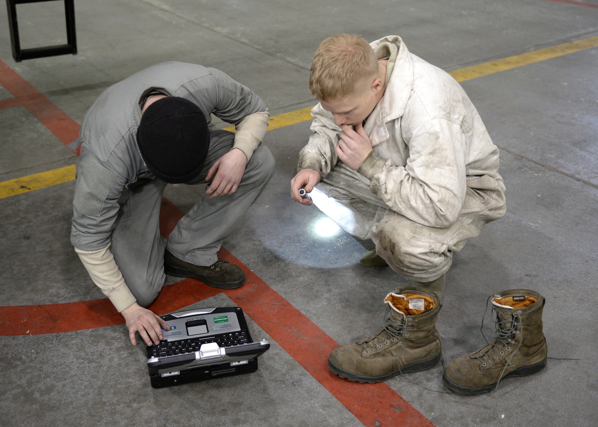 U.S. Air Force Airman 1st Class David Van Hoomissen (left), a 354th Aircraft Maintenance Squadron crew chief, and Senior Airman Jarrod Decker, a 354th AMXS engine technician, go over technical orders for an F-16 Fighting Falcon fighter aircraft at Eielson Air Force Base, Alaska, Nov. 12, 2014. Decker removed his boots and donned protective gear prior to climbing inside the intake of the aircraft to check for defects prior to an engine test. (U.S. Air Force photo by Staff Sgt. Shawn Nickel/Released)