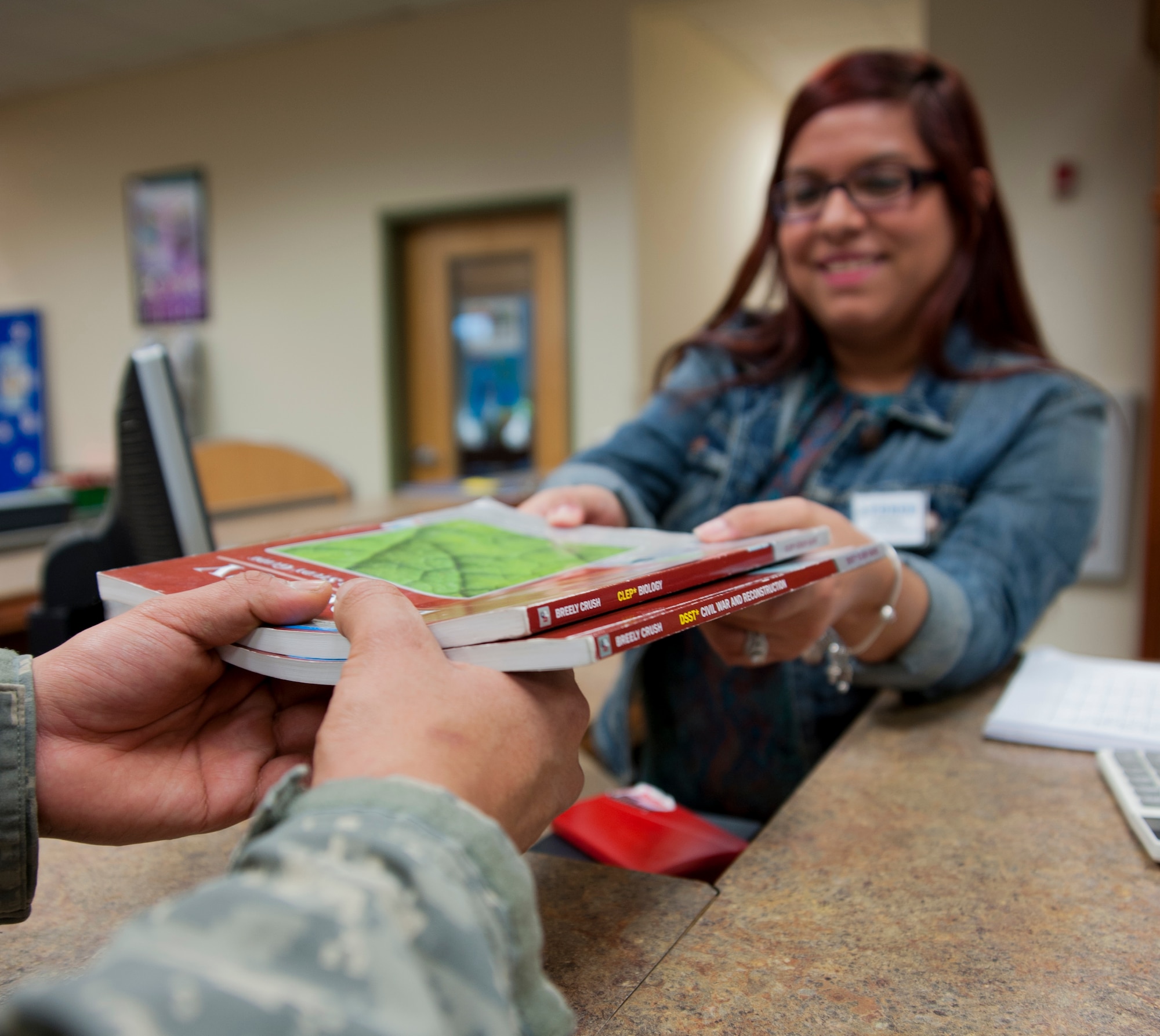A Soldier takes CLEP and DANTE books from Christina Nelson, so he can test out of a college class to be closer to his Associate’s degree Nov. 14, 2014. CLEP and DANTE’s testing is one way to test out of some of the many required subjects a military member needs to complete to earn an Associate’s degree. The education centers and JBER Library provide study materials for those who plan on testing through the CLEP or DANTE’s system. Nelson is assigned to the 673d Force Support Squadron as a library technician. (U.S. Air Force photo/Airman 1st Class Tammie Ramsouer)