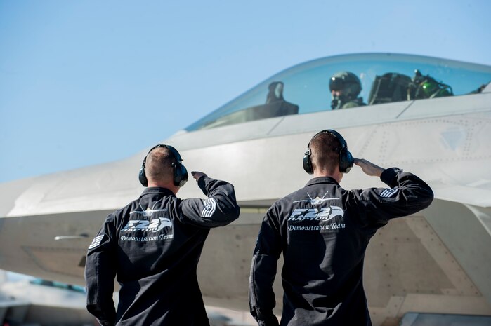 Tech. Sgt. Harrison Southworth (left), an Air National Guard F-22 Raptor dedicated crew chief from the 192nd Aircraft Maintenance Squadron, Joint Base Langley-Eustis, Va., and Staff Sgt. Justin Hubbard, an F-22 dedicated crew chief from the 1st Fighter Wing, Joint Base Langley-Eustis, Va., salute F-22 Demo Team commander Capt. John Cummings, from Joint Base Langley-Eustis, Va., as he taxis to the runway during the open house at Nellis AFB, Nev., Nov. 7, 2014. These Airmen are part of the F-22 Demonstration Team that shows off the maneuvering capabilities of the F-22 at air shows. (U.S. Air Force photo by Airman 1st Class Thomas Spangler)