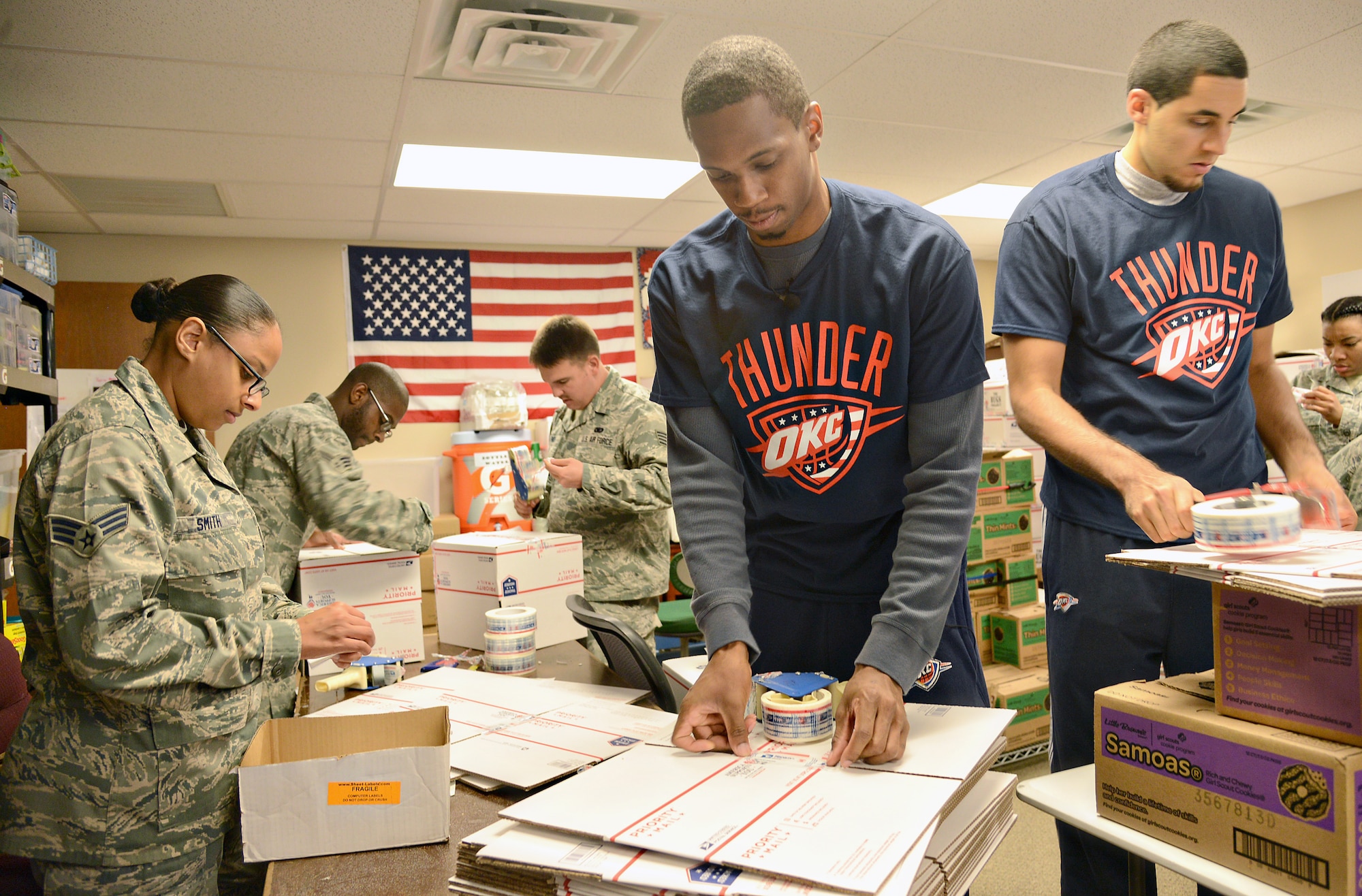 From left, Senior Airmen Petra and Arsenio Smith and Staff Sgt. Dylan Finch work together with Oklahoma City Thunder players Lance Thomas and Grant Jerrett to assemble boxes to be turned into goodie-stuffed care packages for deployed military troops. (Air Force photo by Kelly White)