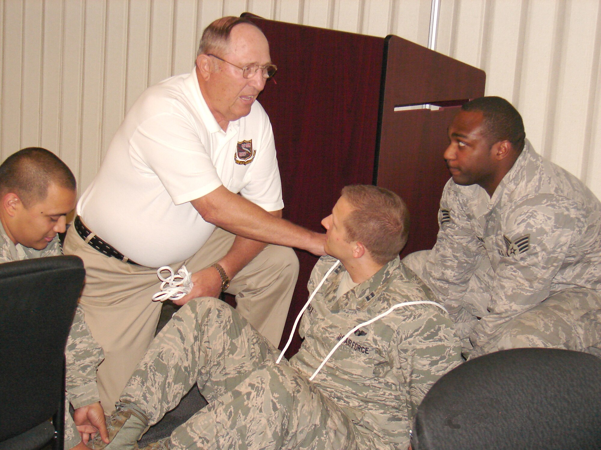 During a speech at the Oklahoma City Air Logistics Complex, retired Col. Leroy W. Stutz demonstrates one of the torture techniques used on him during the more than six years he spent as a prisoner of war during Vietnam.  Assisting in the demonstration are, from left, Staff Sgt. Fermin Cabrera, 545th PMXS/MXDPA; Capt. Robert Mullinax, OC-ALC executive officer; and Staff Sgt. James Gilreath, 76th PMXG/MXDPA. Colonel Stutz, an Air Force pilot, was held prisoner for 2,284 days. (Air Force photo by Staff Sgt. John P. Gudino)