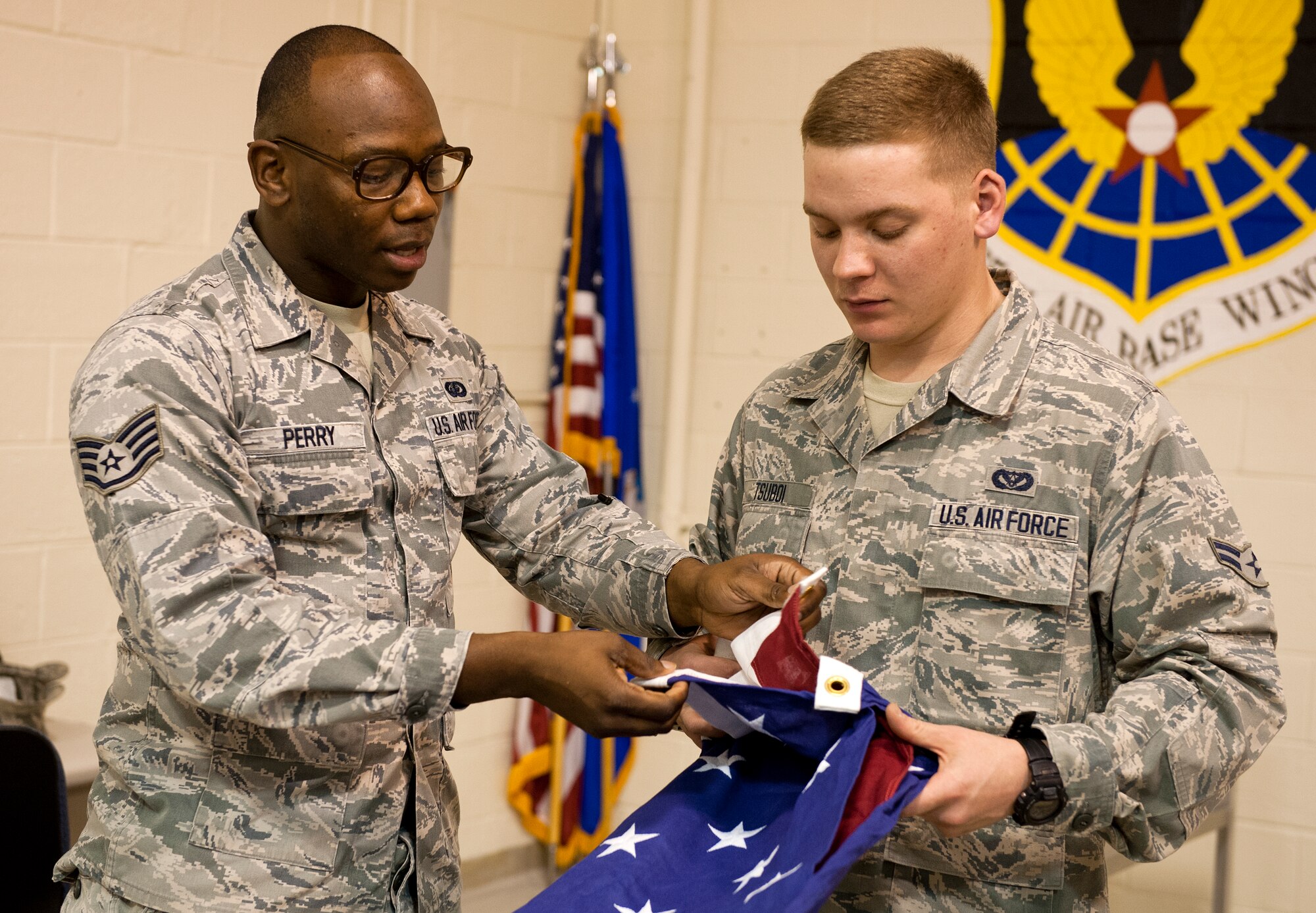 Staff Sgt. Monteco Perry, 65th Air Base Wing Honor Guard non-commissioned officer in charge, shows Airman 1st Class Anthony Tsuboi, a heating, ventilating and air conditioning technician with the 65th Civil Engineer Squadron, flag folding techniques at Lajes Field, Azores, Portugal, Nov. 13, 2014. A ceremonial guardsman is an individual of good reputation, having integrity, ethical conduct and exhibiting standards which merit respect; responsible for protecting and overseeing the maintenance of standards on and off duty. (U.S. Air Force photo/Staff Sgt. Zachary Wolf/Released)