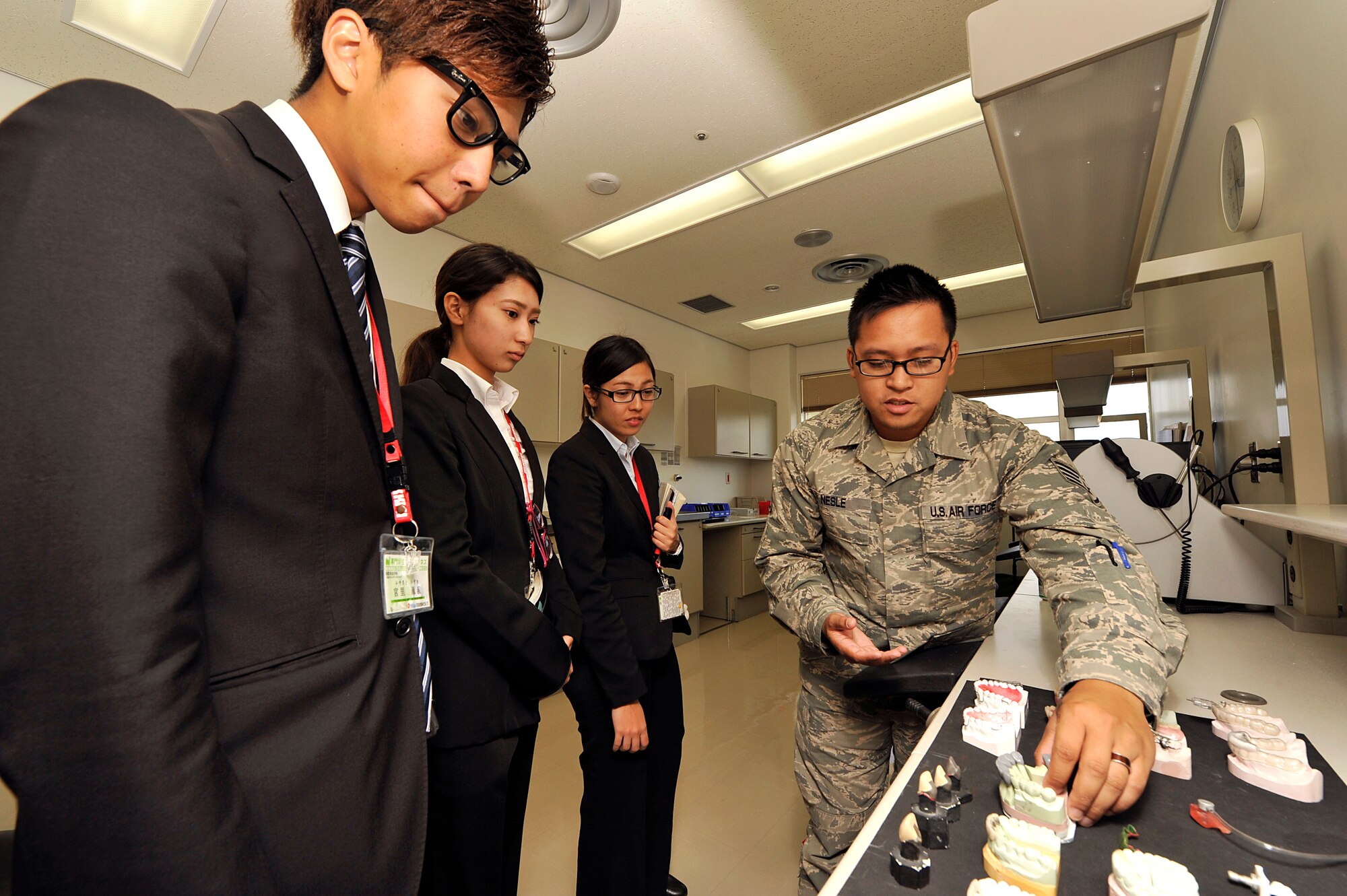 U.S. Air Force Staff Sgt. Jet Nesle, 18th Dental Squadron NCO in charge of radiology, shows teeth molds to students from the Nikkei College of Business in Okinawa City during a base facility tour on Kadena Air Base, Japan, Nov. 14, 2014. The program allows the U.S. military to support the local community by hosting a program for local students to help improve their English skills. (U.S. Air Force photo/Naoto Anazawa)