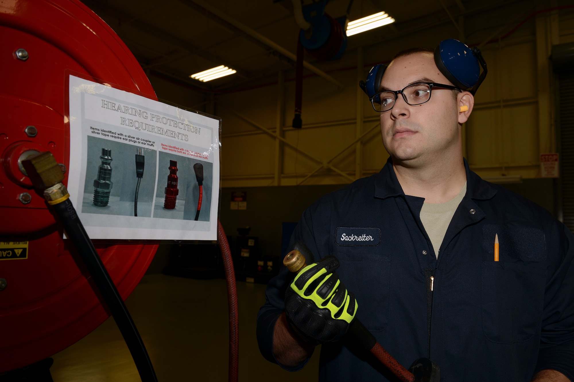 Staff Sgt. Anthony Sackreiter, 627th Logistics Readiness Squadron vehicle maintenance journeyman, pulls an air hose while he glances at the hearing protection requirements poster Nov. 5, 2014, at Joint Base Lewis-McChord, Wash. These posters were put around work areas that require hearing protection to remind workers to have the proper protective equipment. (U.S. Air Force photo/Airman 1st Class Keoni Chavarria)