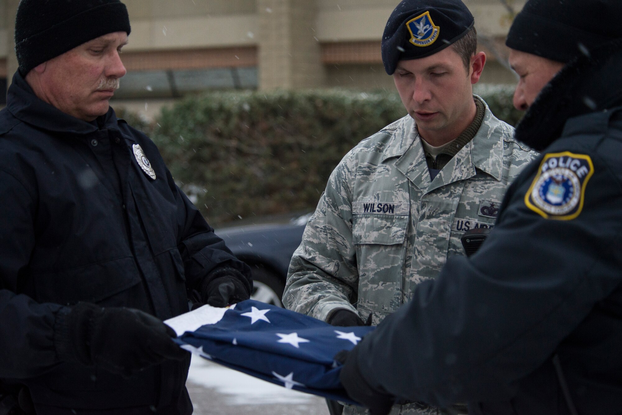 Two Department of the Air Force police officers and one member of the 366th Security Forces Squadron work together to fold the flag at Mountain Home Air Force Base, Idaho, Nov. 13, 2014. The three men performed the retreat in freezing cold temperatures and the first snow of the year. (U.S. Air Force photo by Airman 1st Class Jessica H. Smith/RELEASED)  