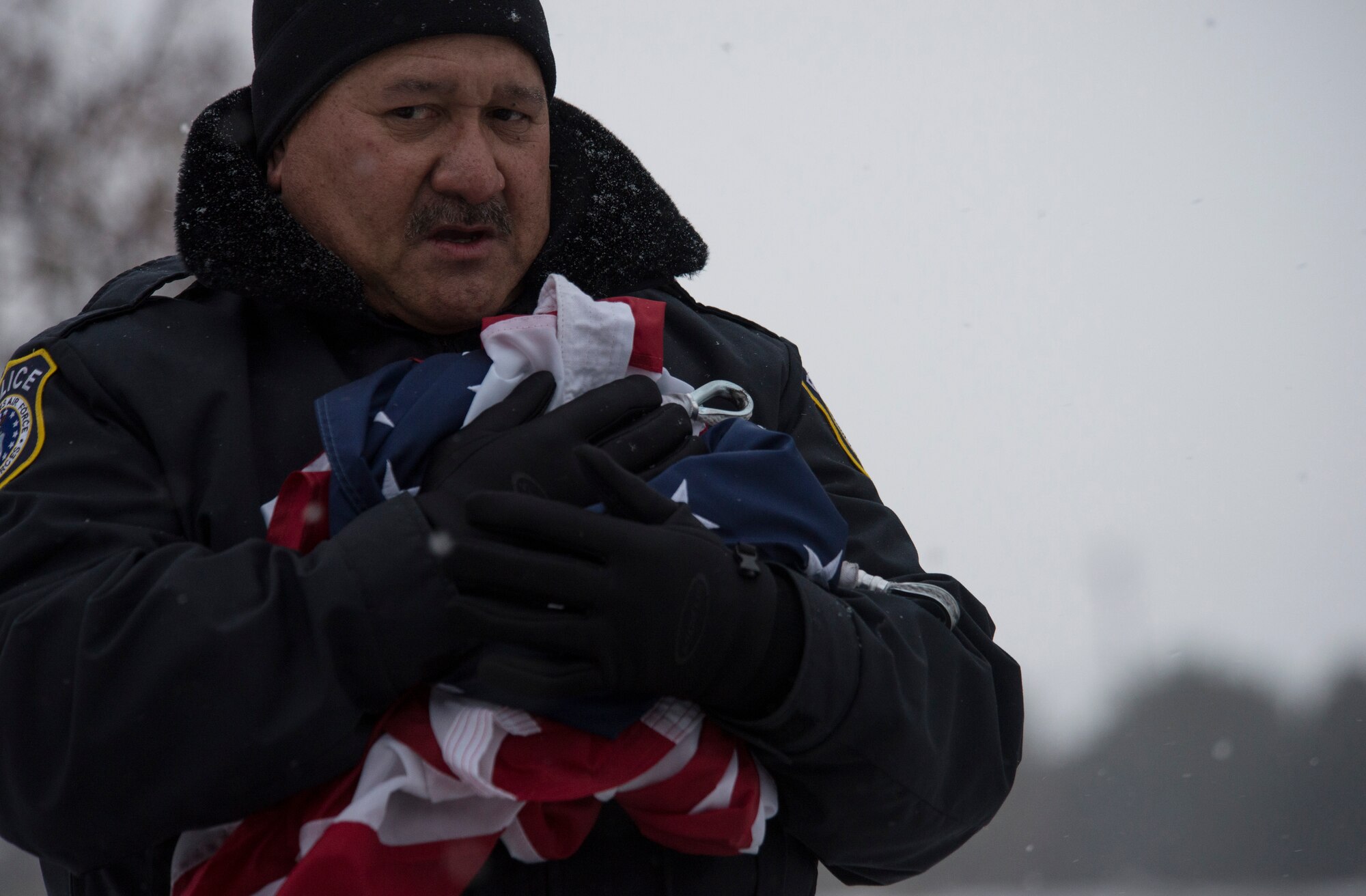 Officer Glenn Reyes, Department of the Air Force police officer, catches and holds the flag after it is lowered at Mountain Home Air Force Base, Idaho, Nov. 13, 2014. Despite the falling snow, Reyes still performed as necessary to make sure the flag came down correctly. (U.S. Air Force photo by Airman 1st Class Jessica H. Smith/RELEASED)