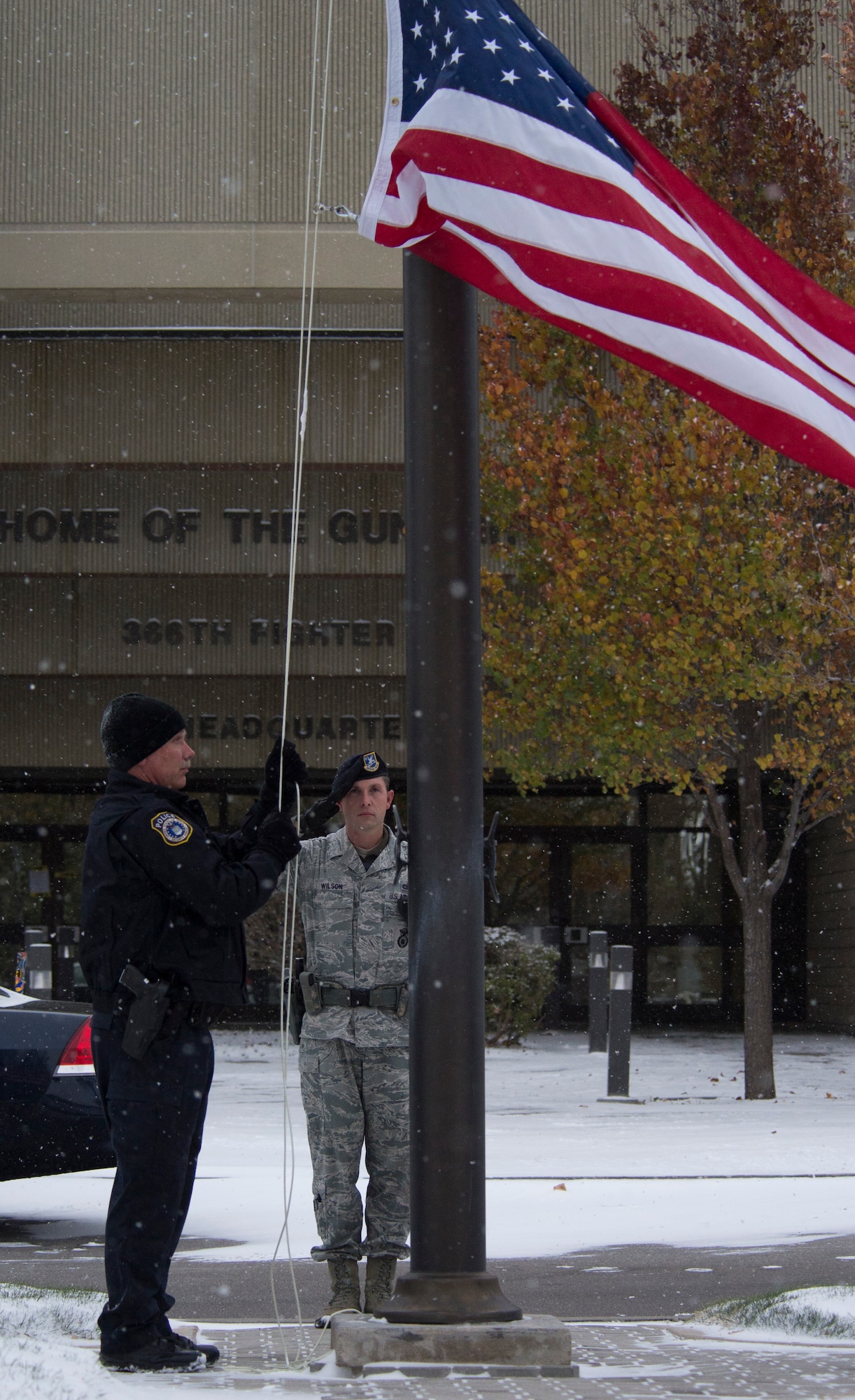 Tech. Sgt. Robert Wilson, 366th Security Forces Squadron flight chief, salutes the flag as Officer Robert Hendrick, Department of the Air Force police officer, slowly lowers it at Mountain Home Air Force Base, Idaho, Nov. 13, 2014. Despite the extreme cold weather and snow the men still performed retreat as they would any other day. (U.S. Air Force photo by Airman 1st Class Jessica H. Smith/RELEASED)