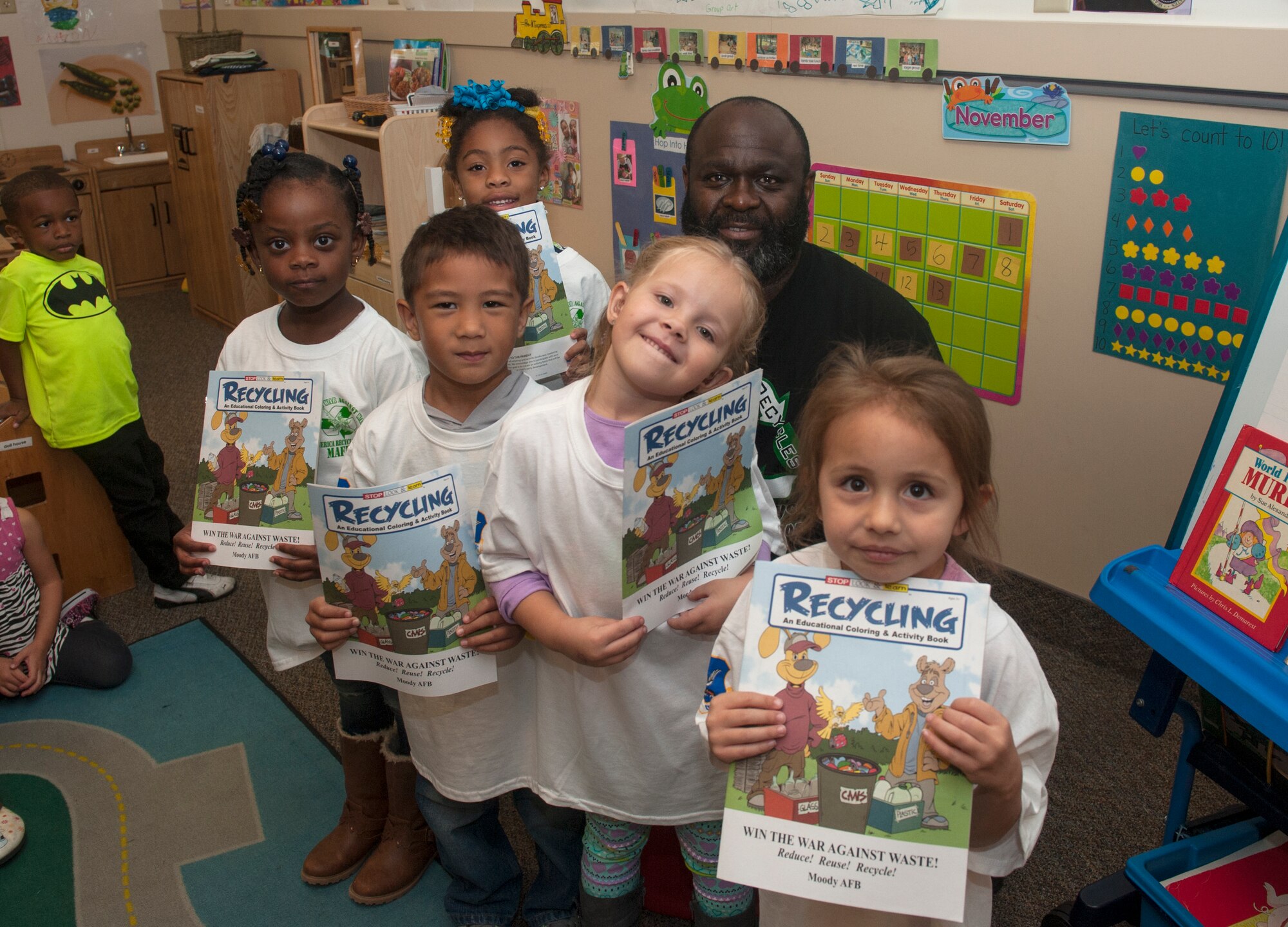 Elvis Lane, back center, 23d Civil Engineer Squadron environmental specialist, poses with children during an America Recycles Day visit to the Child Development Center Nov. 13, 2014, at Moody Air Force Base, Ga. Lane handed out America Recycles Day shirts and coloring books to help teach them about recycling. (U.S. Air Force photo by Senior Airman Jarrod Grammel/Released)
