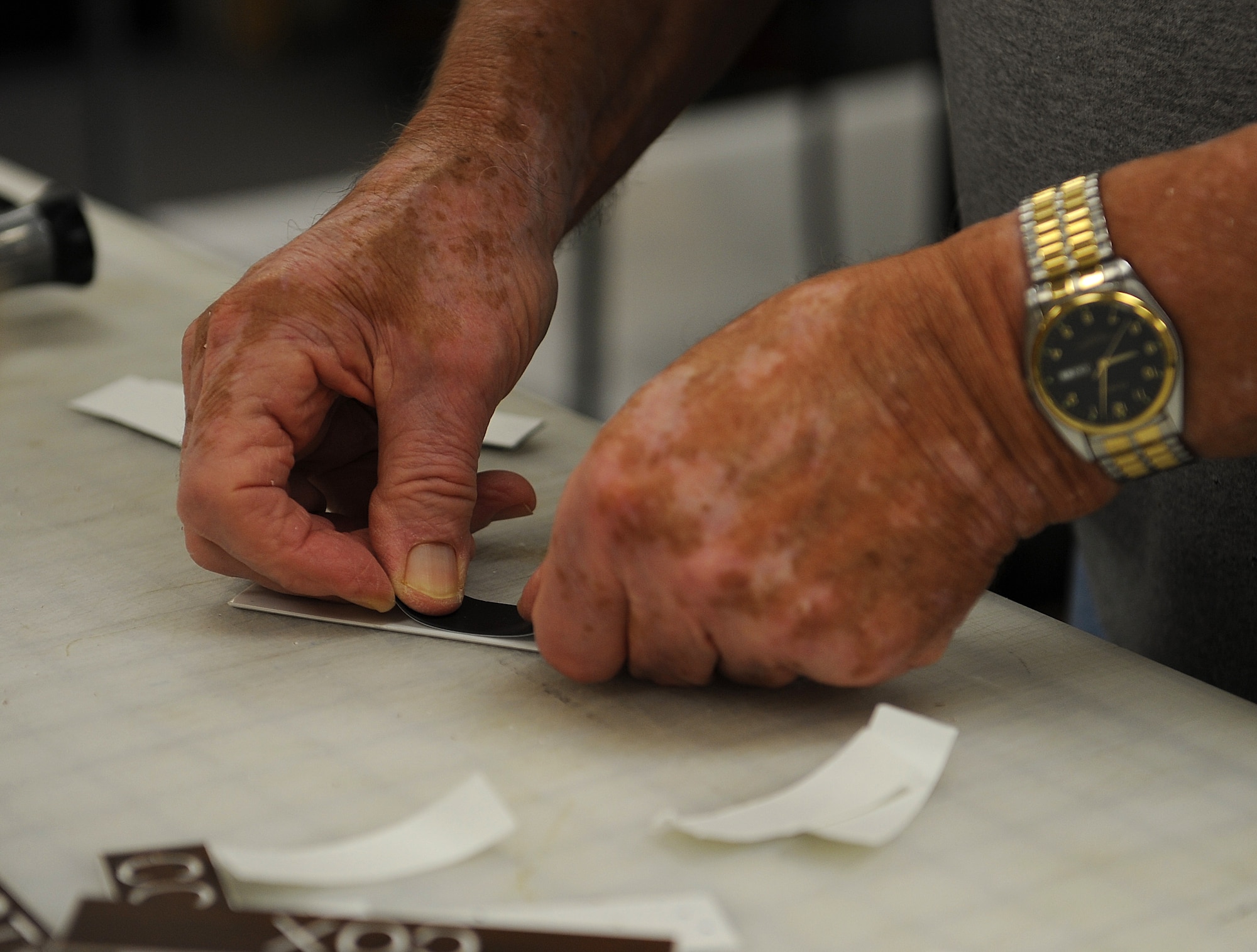 Terry Lee, K-Mar Industries illustrator, puts a magnet on the back of a name plate Nov. 10, 2014, Keesler Air Force Base, Miss. Lee has dedicated more than 20 years of service to the Air Force since he started out as a B-52 Stratofortress maintainer in 1962 at McCoy Air Force Base, Florida. He now works as a contractor for the military making graphics, informative posters and engraving. (U.S. Air Force photo/Senior Airman Holly Mansfield)