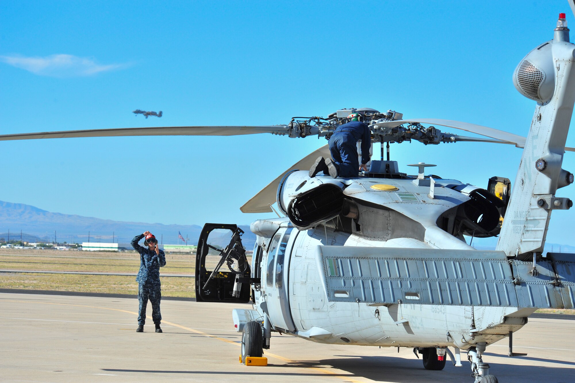 Sailors detached from Helicopter Sea Combat Squadron 4,Naval Air Station North Island, San Diego, Calif., perform preflight checks on a Navy MH-60S Knighthawk as an A-10C Thunderbolt II flies in the background at Davis-Monthan Air Force Base, Ariz., Nov. 13, 2014.  HSC-4 conducted joint training with D-M A-10C Thunderbolt II squadrons and Combat Search and Rescue units to strengthen operations between the services.  (U.S. Air Force Photo by Airman 1st Class Chris Massey/Released)