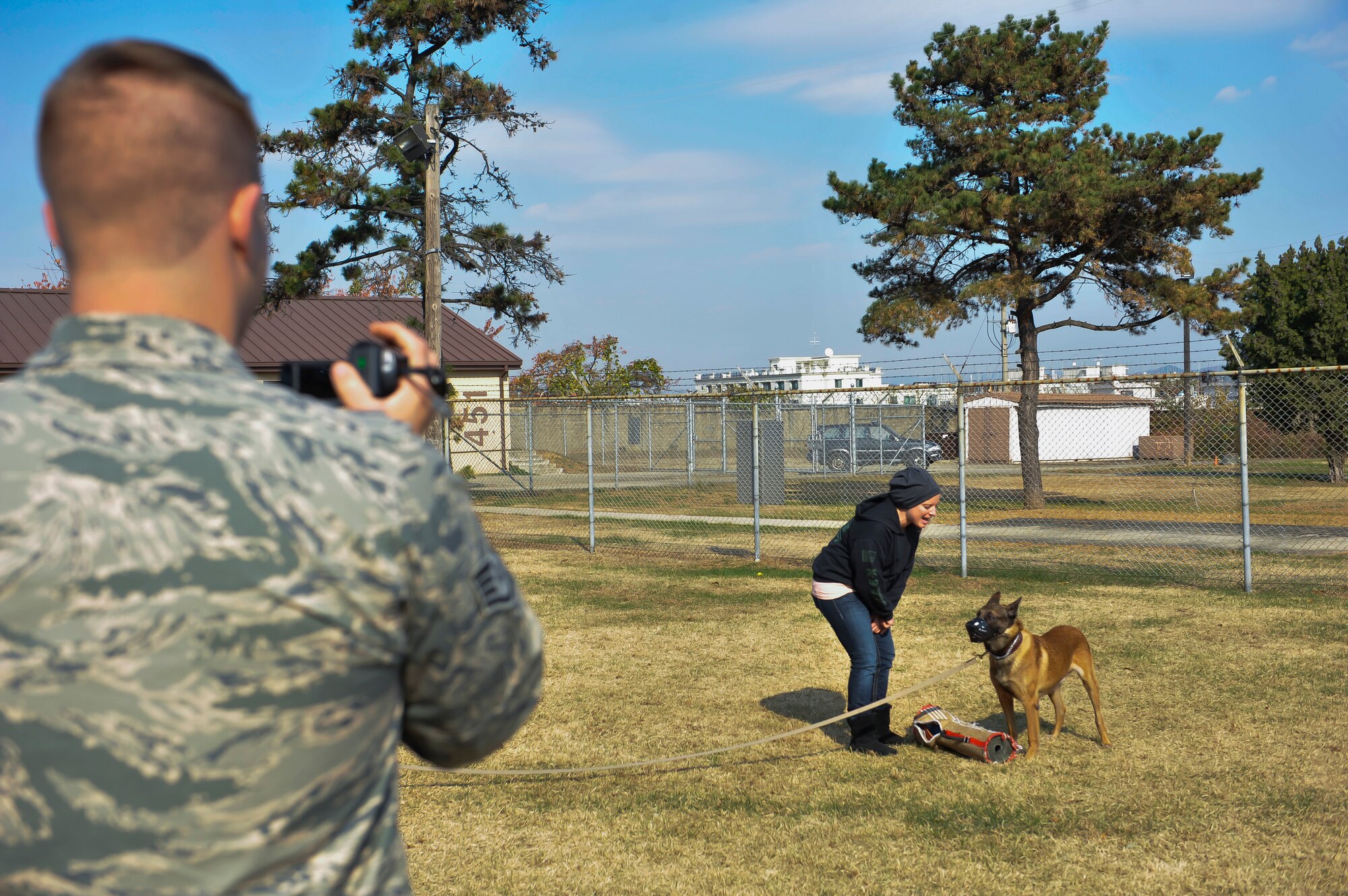 Staff Sgt. Brian Brady, 51st Security Forces Squadron military working dog handler, takes video of Staff Sgt. Anique Brassard, 51st SFS MWD handler, yelling at Fficher, 51st SFS MWD, during part of the adoption process Nov. 14, 2014, on Osan Air Base, Republic of Korea. The video is created to show that the dog has no tendencies to aggress and it suitable for pet adoption. (U.S. Air Force photo by Senior Airman David Owsianka)