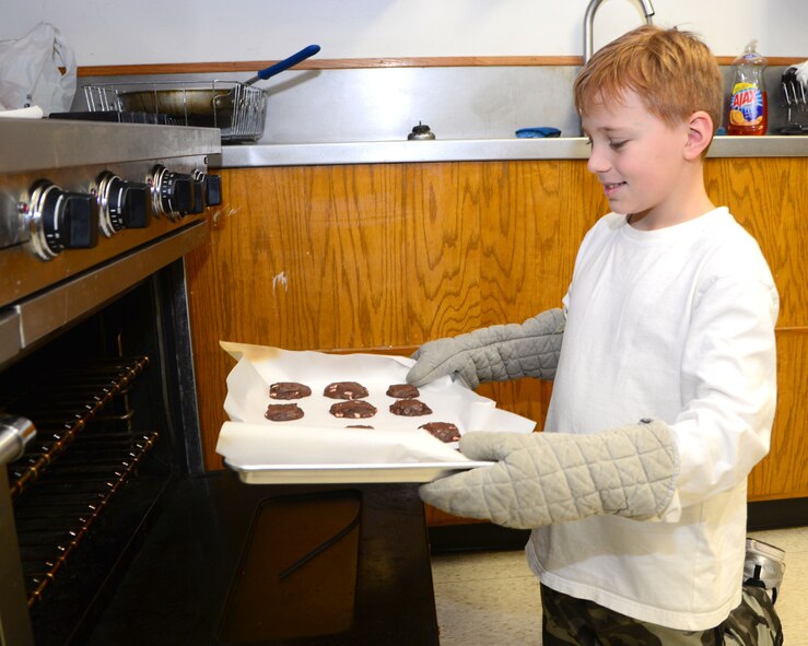 VANCE AIR FORCE BASE, Okla. -- Jack Cinnamon, son of Col.  John Cinnamon, the 71st Operations Group commander, pulls out freshly-baked cookies from and oven during Operation Cookie Cutter in the Community Chapel Activity Center Nov. 14. For more than 20 years, members of Team Vance have mailed cookies and other sweets to deployed Vance Airmen. Twenty-two boxes filled with about 150 cookies each will make their way to Team Vance’s deployed warriors. (U.S. Air Force photo/Senior Airman Frank Casciotta)