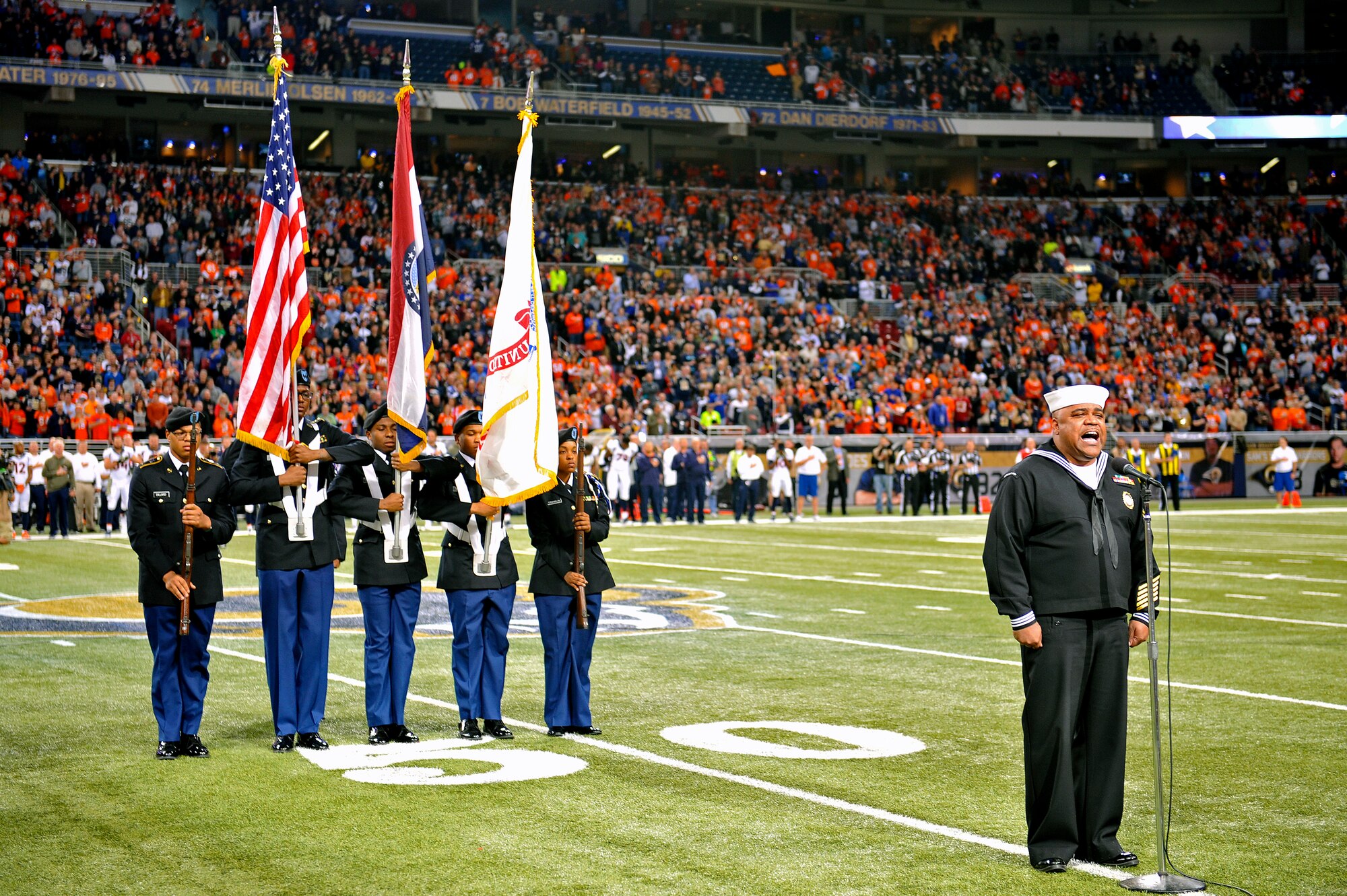 A U.S. Navy servicemember sings the National Anthem with the Army ROTC honor guard presenting the colors at Military Appreciation Day's pregame ceremony. The St. Louis Rams went up against the Denver Broncos in the Edward Jones Dome, St. Louis, Nov. 16, 2014. The day included honoring wounded warriors and honor guards from every branch of the Armed Forces presented the colors. The Rams won 7-22. (U.S. Air Force photo by Airman 1st Class Erica Crossen)