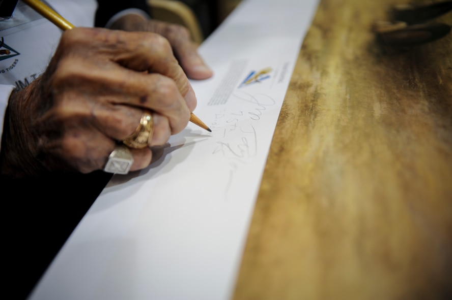 J.M. Taylor, former 75th Fighter Squadron pilot and World War II veteran, signs a painting depicting WWII weapons troops in action after the 2014 Flying Tigers Reunion dinner Nov. 15, 2014, in Valdosta, Ga. Taylor was one of three original World War II era Flying Tiger members to attend the event. (U.S. Air Force photo by Andrea Jenkins/Released)