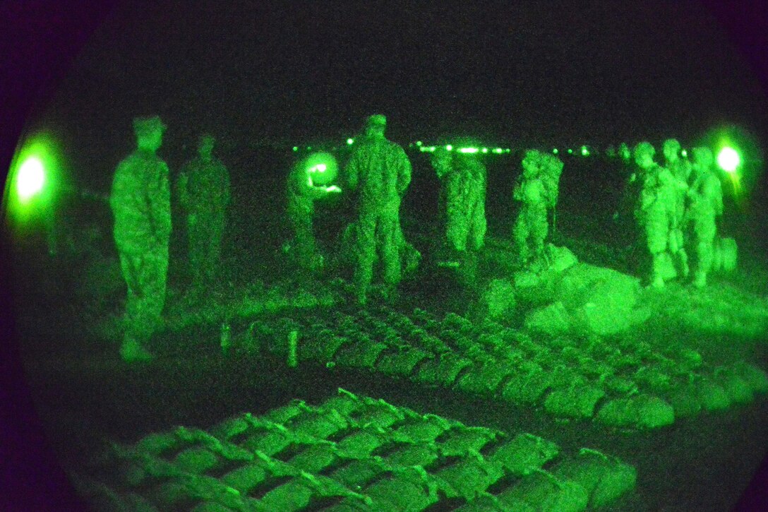 As seen through a night-vision device, U.S. paratroopers receive a mission brief and pick up their parachutes before conducting a night airborne operation from a C-130 Hercules aircraft over Juliet Drop Zone in Pordenone, Italy, Nov. 18, 2014. The paratroopers are assigned to Company B, 2nd Battalion, 503rd Infantry Regiment, 173rd Airborne Brigade.