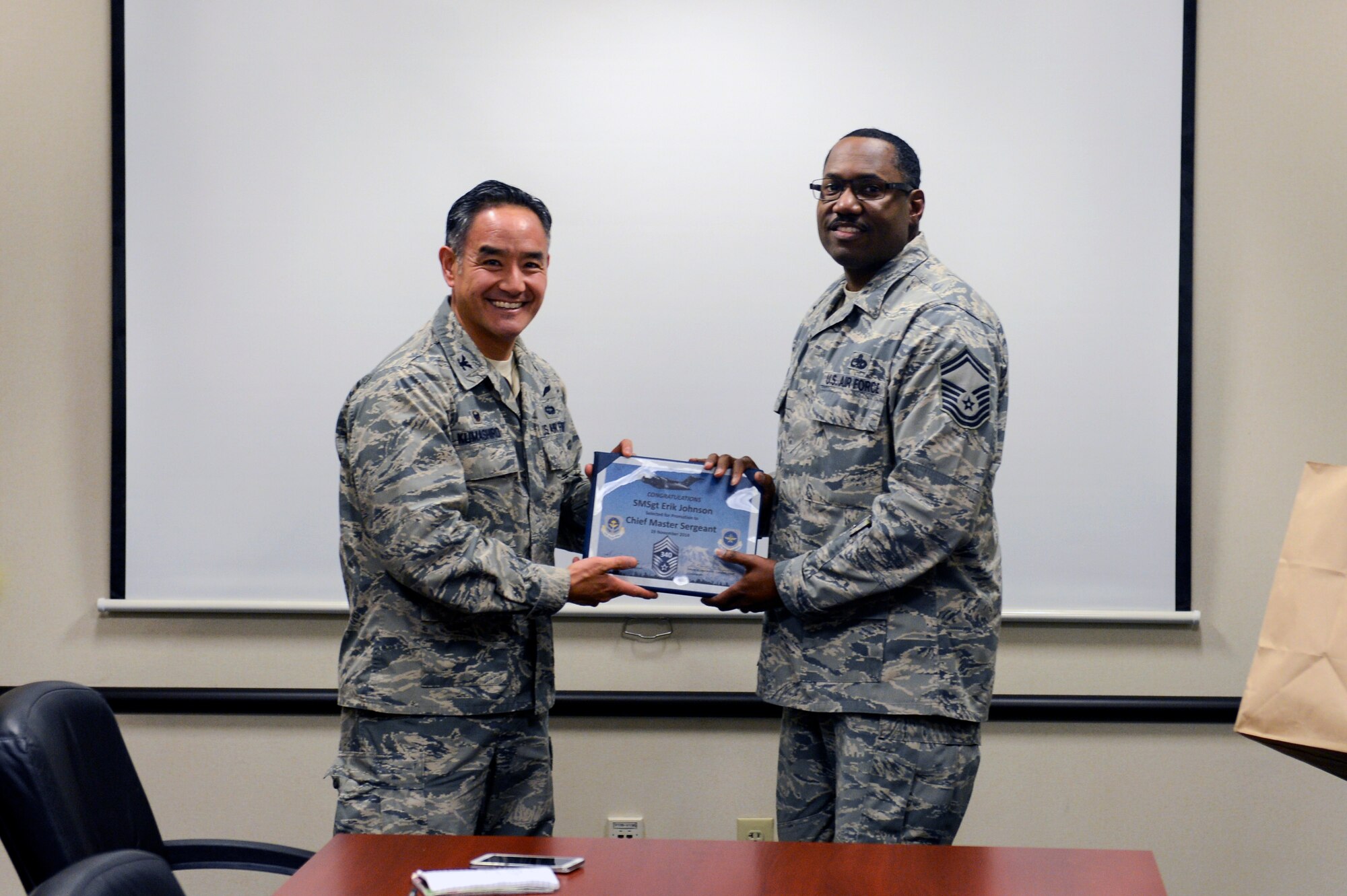 Col. David Kumashiro (left), 62nd Airlift Wing commander, presents Senior Master Sgt. Erik Johnson (right), 62nd Aircraft Maintenance Squadron blue aircraft maintenance unit assistant superintendent, with his promotion certificate to chief master sergeant Nov. 19, 2014, at Joint Base Lewis-McChord, Wash. Johnson was one of three senior master sergeants from McChord Field selected for promotion to chief master sergeant. (U.S. Air Force photo/Staff Sgt. Sam Coleman)
